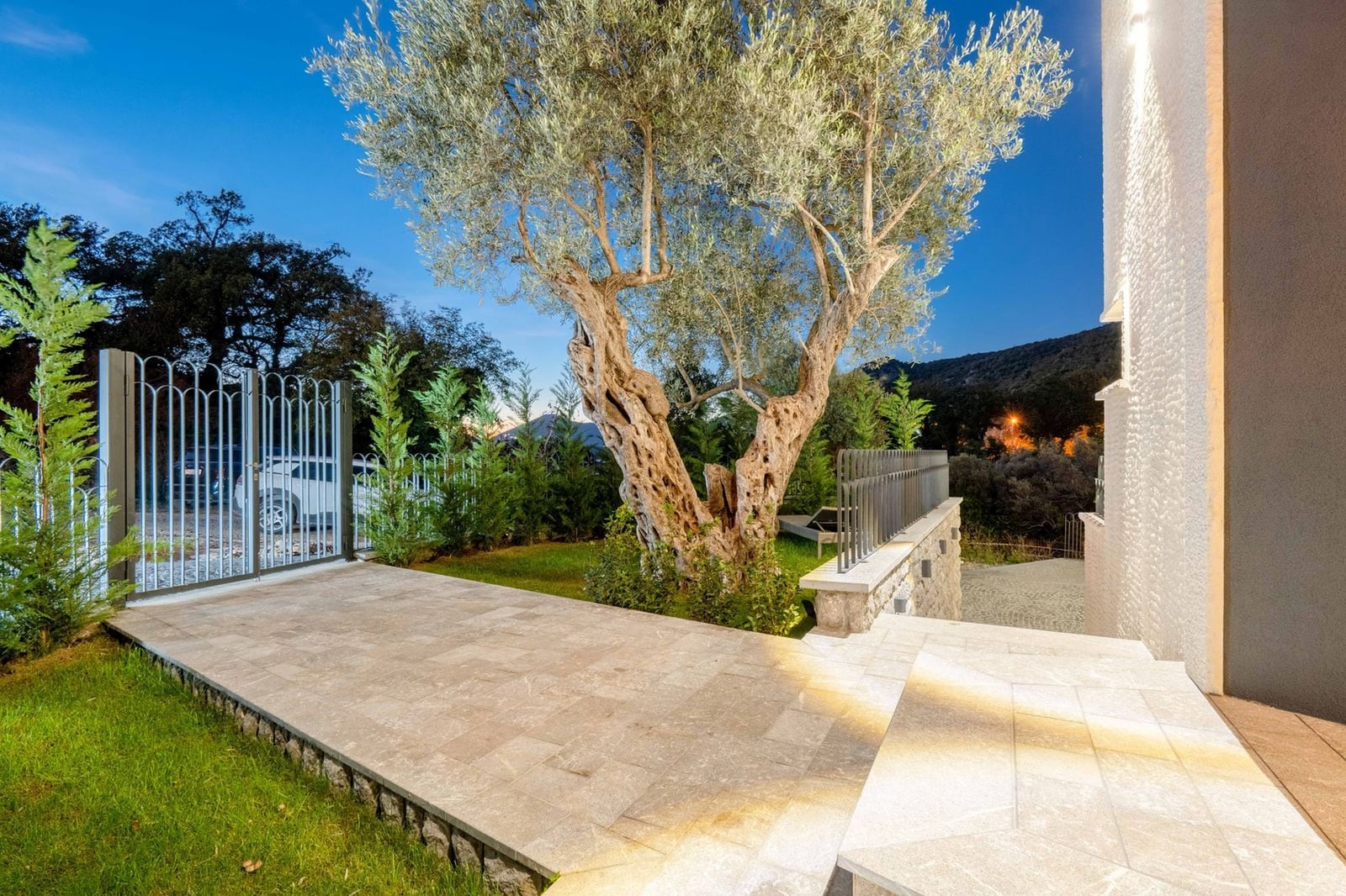 Villa terrace in Kamenovo, Montenegro: stone finish, old olive tree, landscape design, and mountain view in the evening.