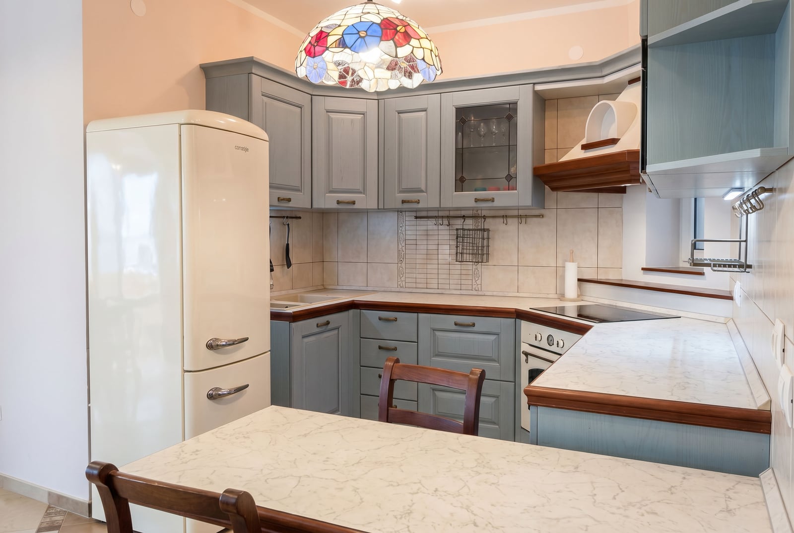 Cozy kitchen in an apartment in Bar, Montenegro: blue cabinetry, vintage refrigerator, and stained-glass chandelier.