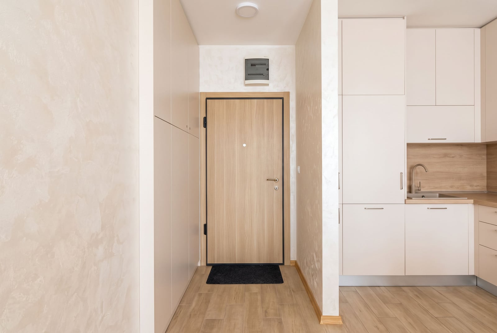 Entryway with a wooden door and partial view of a kitchen featuring white cabinets and a sink.