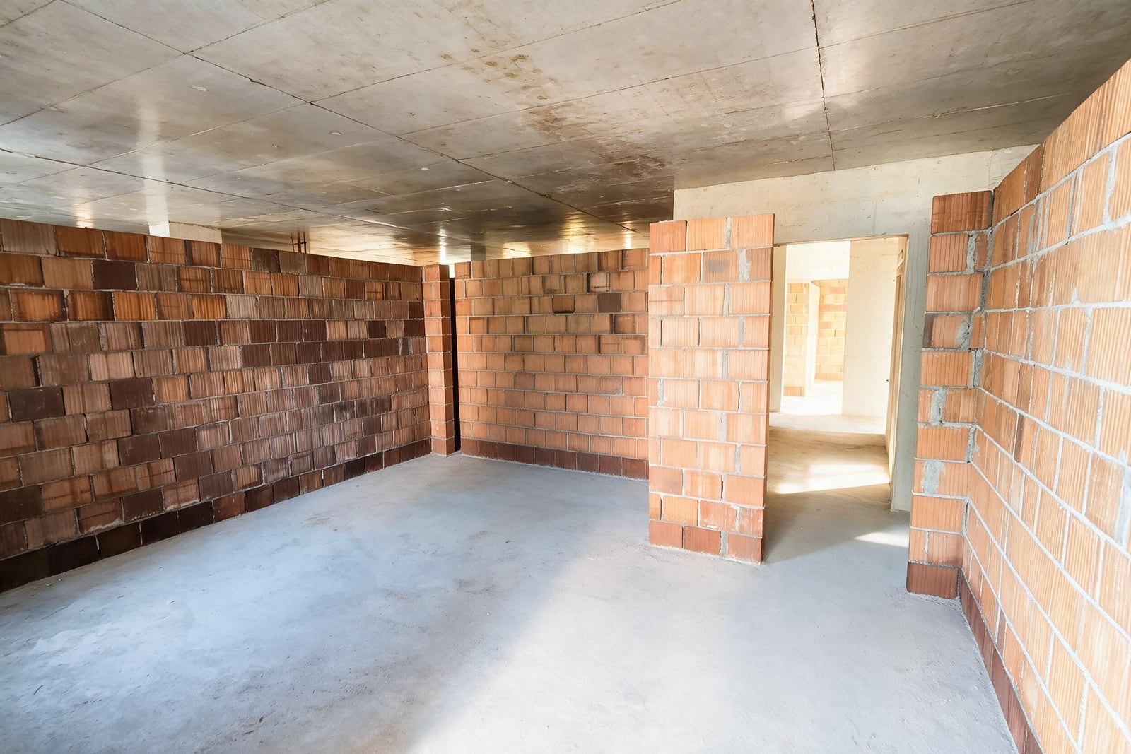 Unfinished construction space with exposed brick walls, concrete ceiling and floor, and an open doorway.
