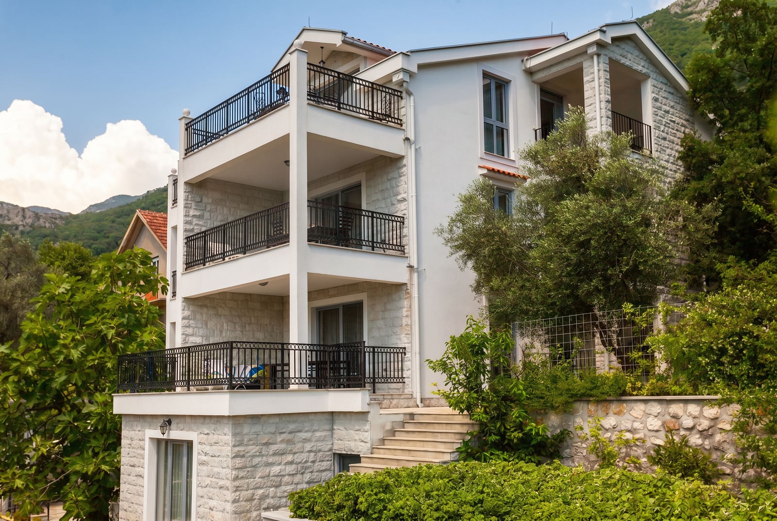 Three-story villa in Risan, Montenegro: white stone facade, spacious terraces with wrought iron railings, and a garden.