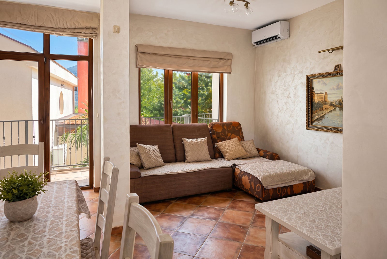 Living room featuring a brown corner sofa, white dining chairs and table on terracotta tiled flooring.