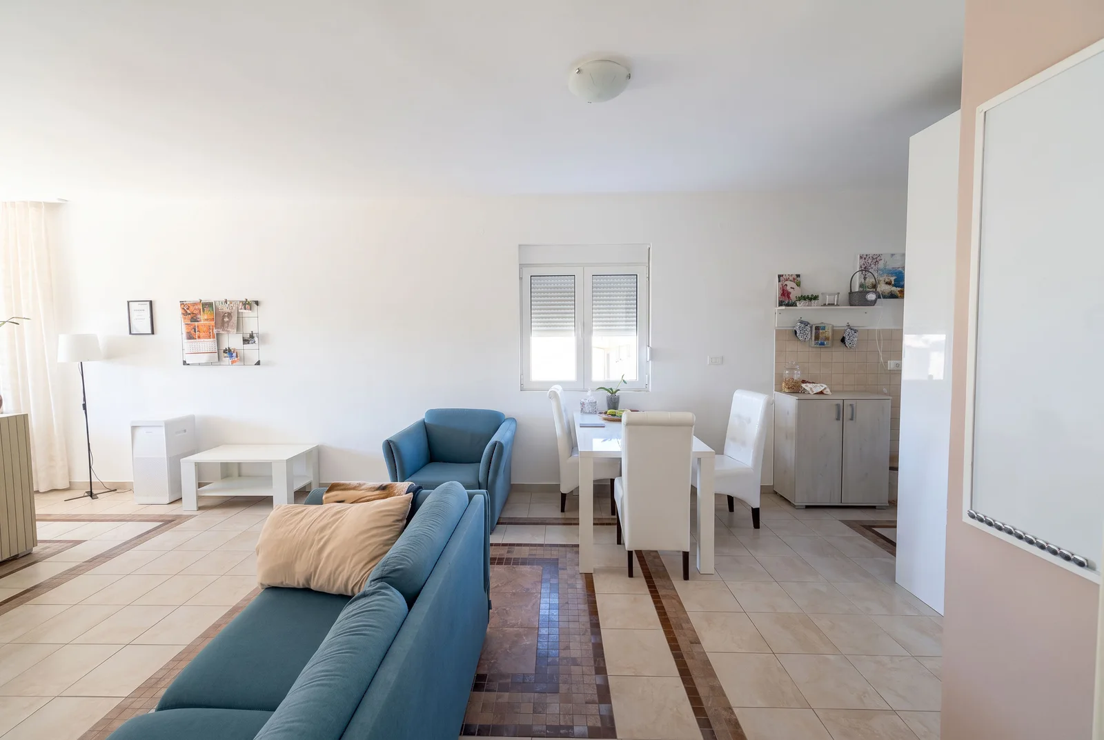 Living room featuring a blue sofa, white dining table with chairs, and tiled flooring.
