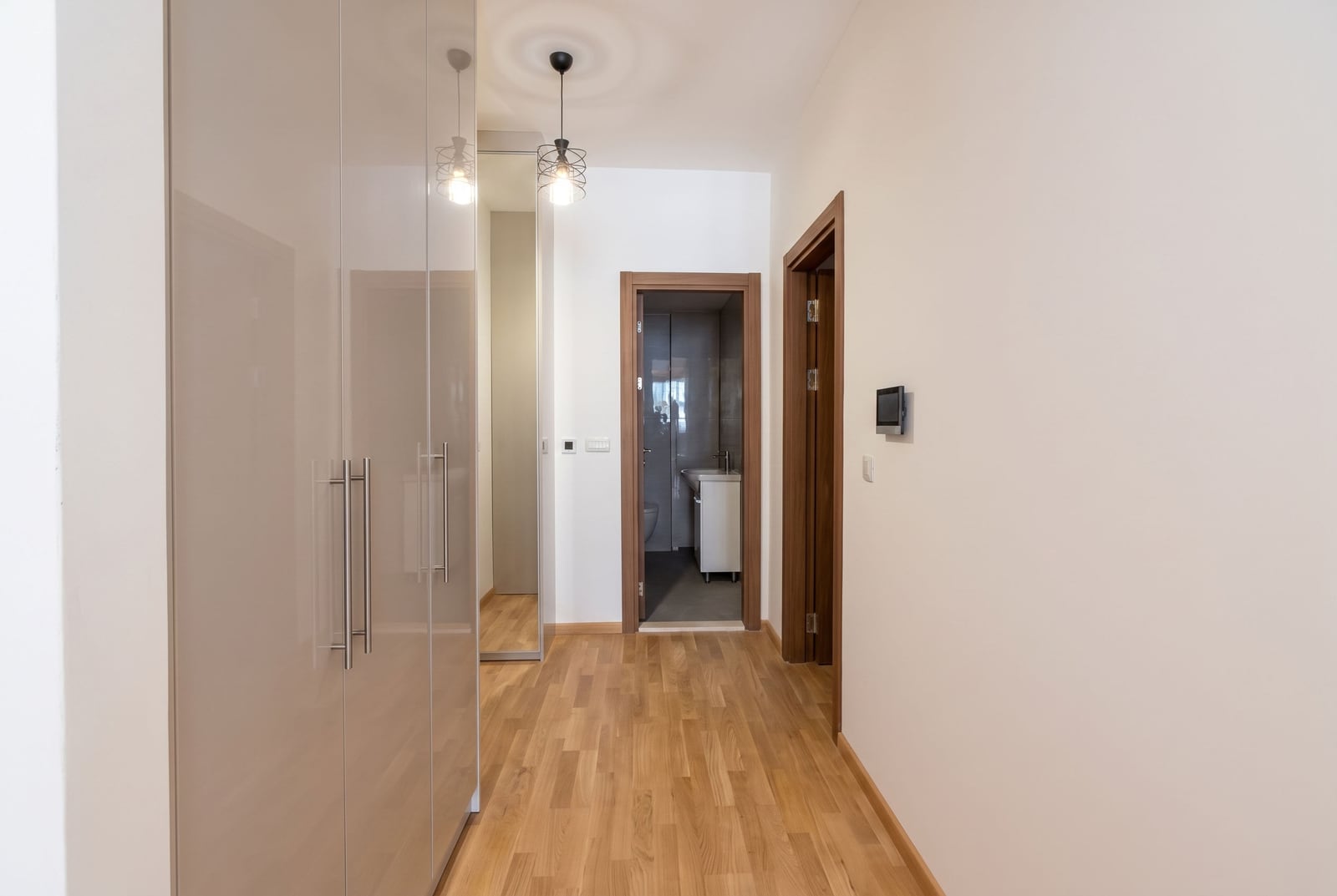 Bright hallway in a Budva apartment, Montenegro: built-in glossy wardrobe, mirror, and entrance to the bathroom.