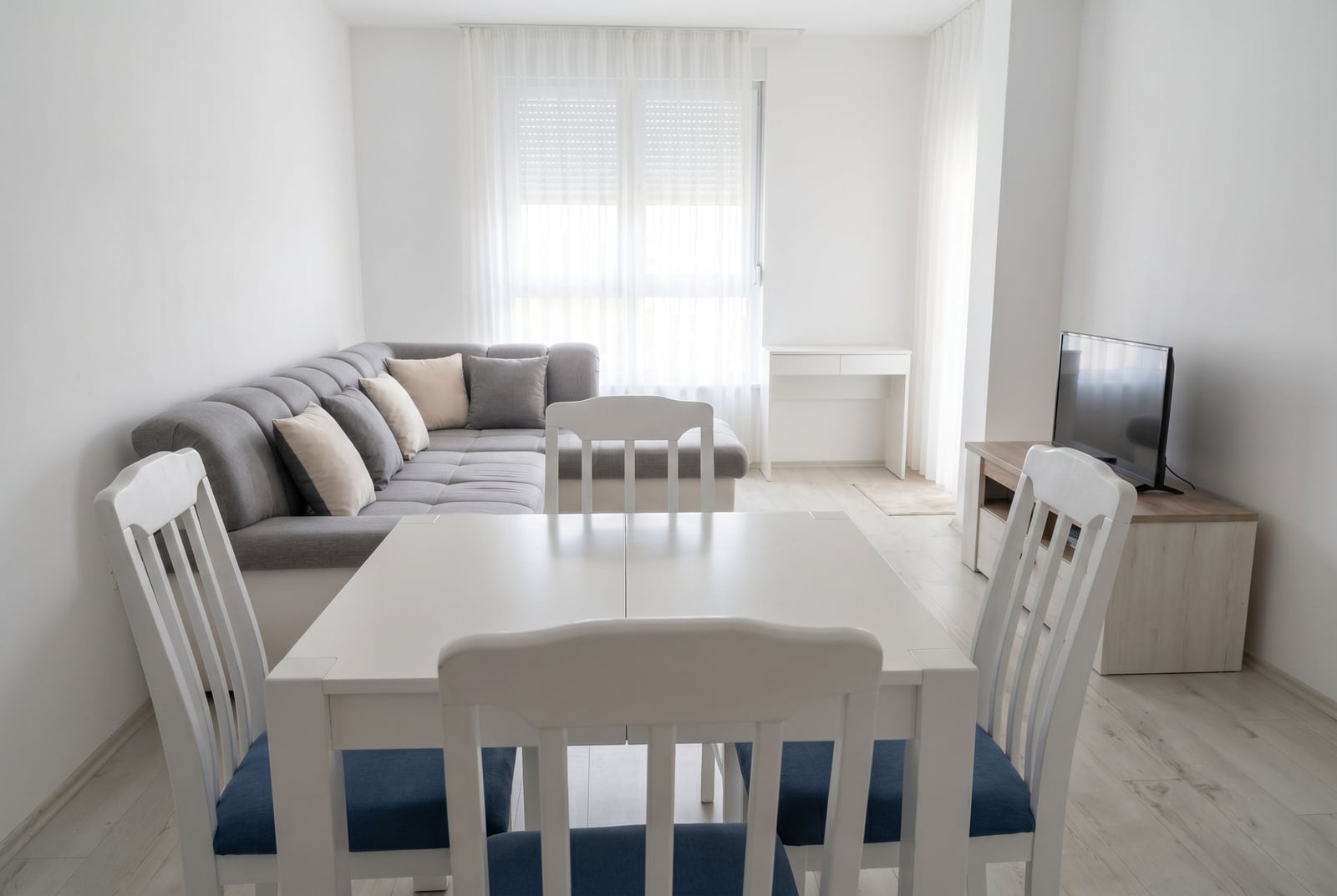 Bright living room with a white dining area, gray corner sofa, and TV in an apartment in Budva, Montenegro