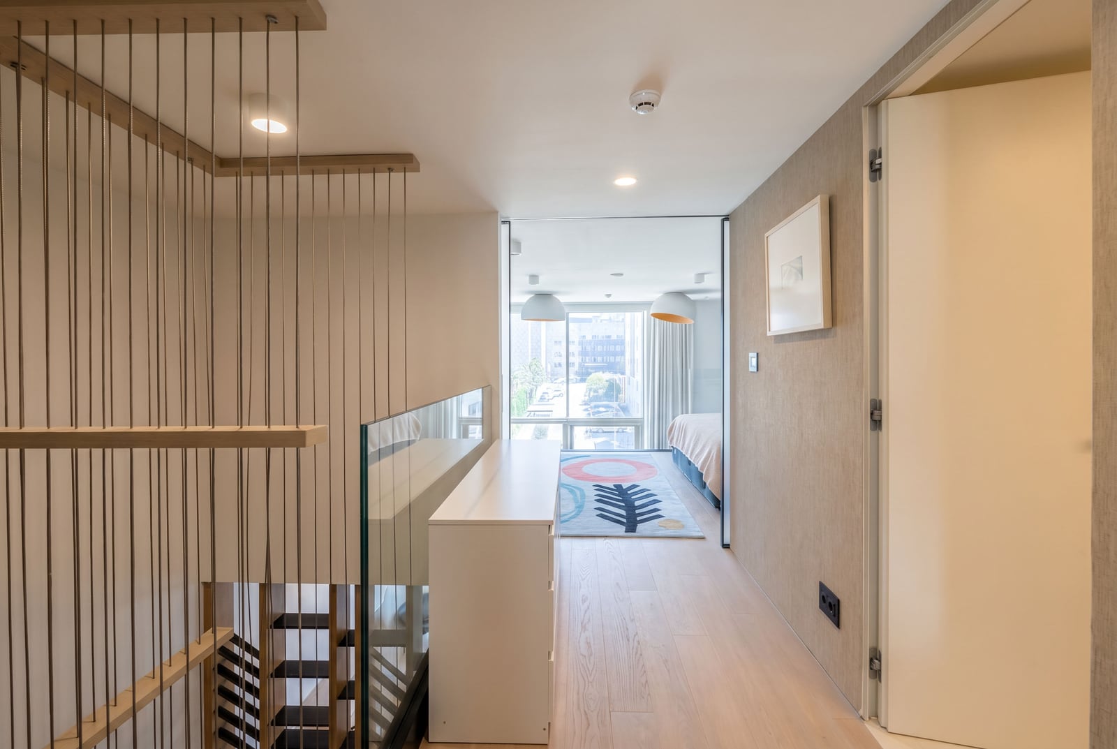 Modern apartment interior in Budva, Montenegro: staircase with cable railing, light-colored flooring, and a view of the bedroom.