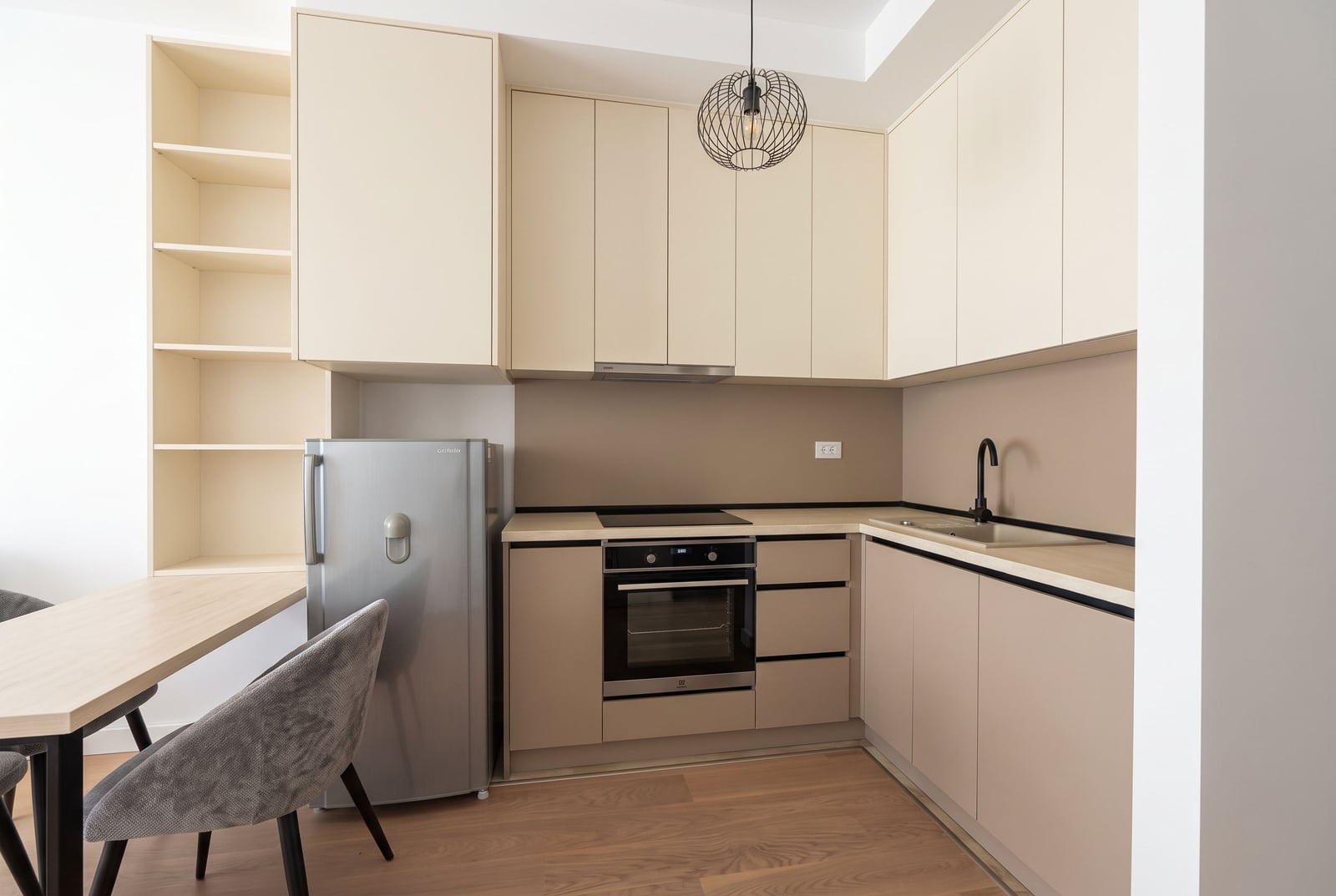 Modern kitchen with beige cabinets, fridge, oven, sink, and a small dining table area.