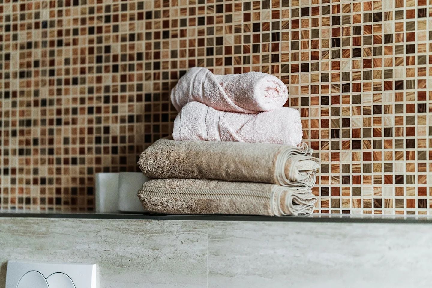 A stack of clean towels in the bathroom of a modern apartment in Budva, Montenegro, finished with mosaic tile.