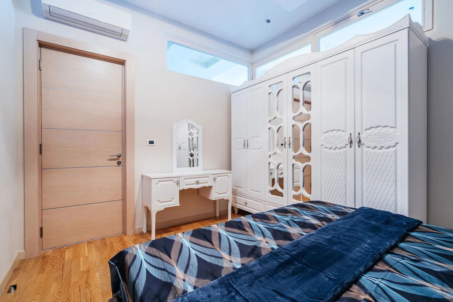 Bedroom in an apartment in Budva, Montenegro: white mirrored wardrobe, vanity table, bed, and parquet floor.