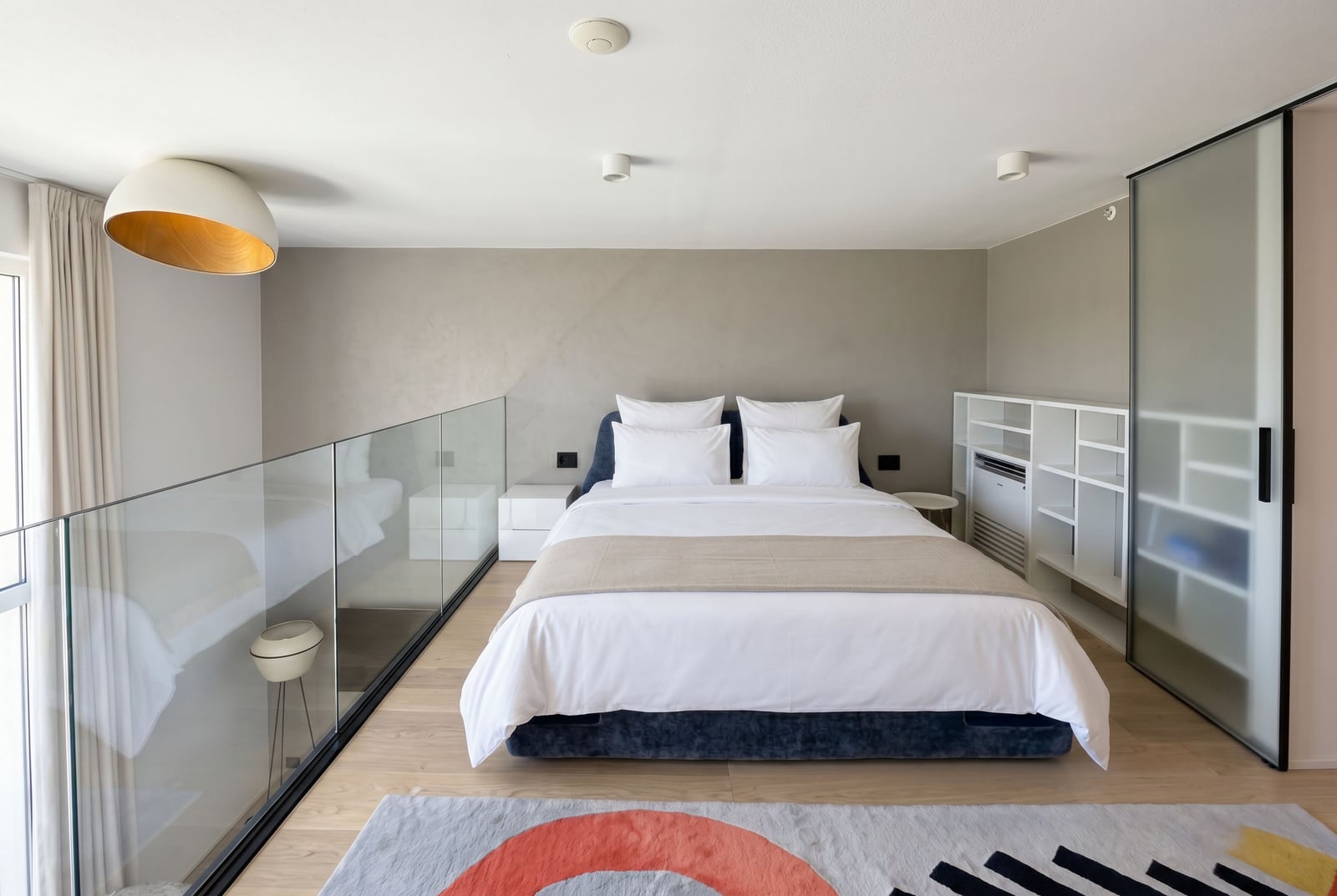 Modern bedroom in a Budva apartment, Montenegro: double bed, glass railing, and stylish interior.