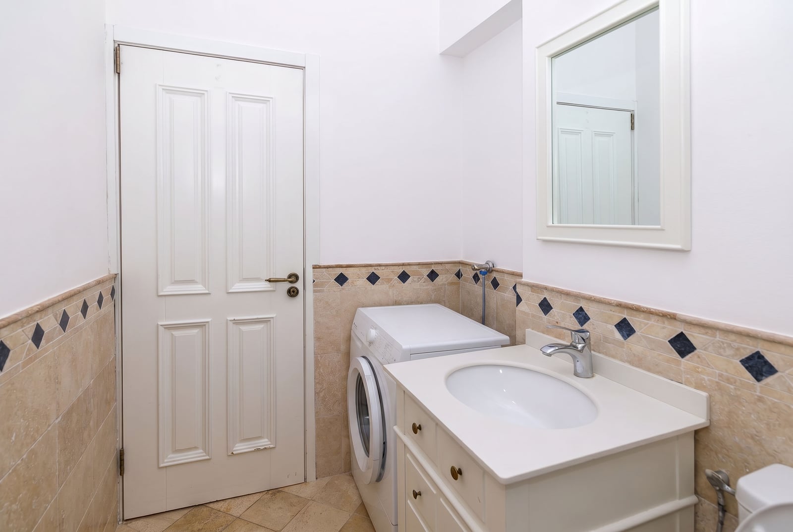 Bright bathroom in an apartment in Risan, Montenegro: white vanity unit with sink, mirror, and washing machine.