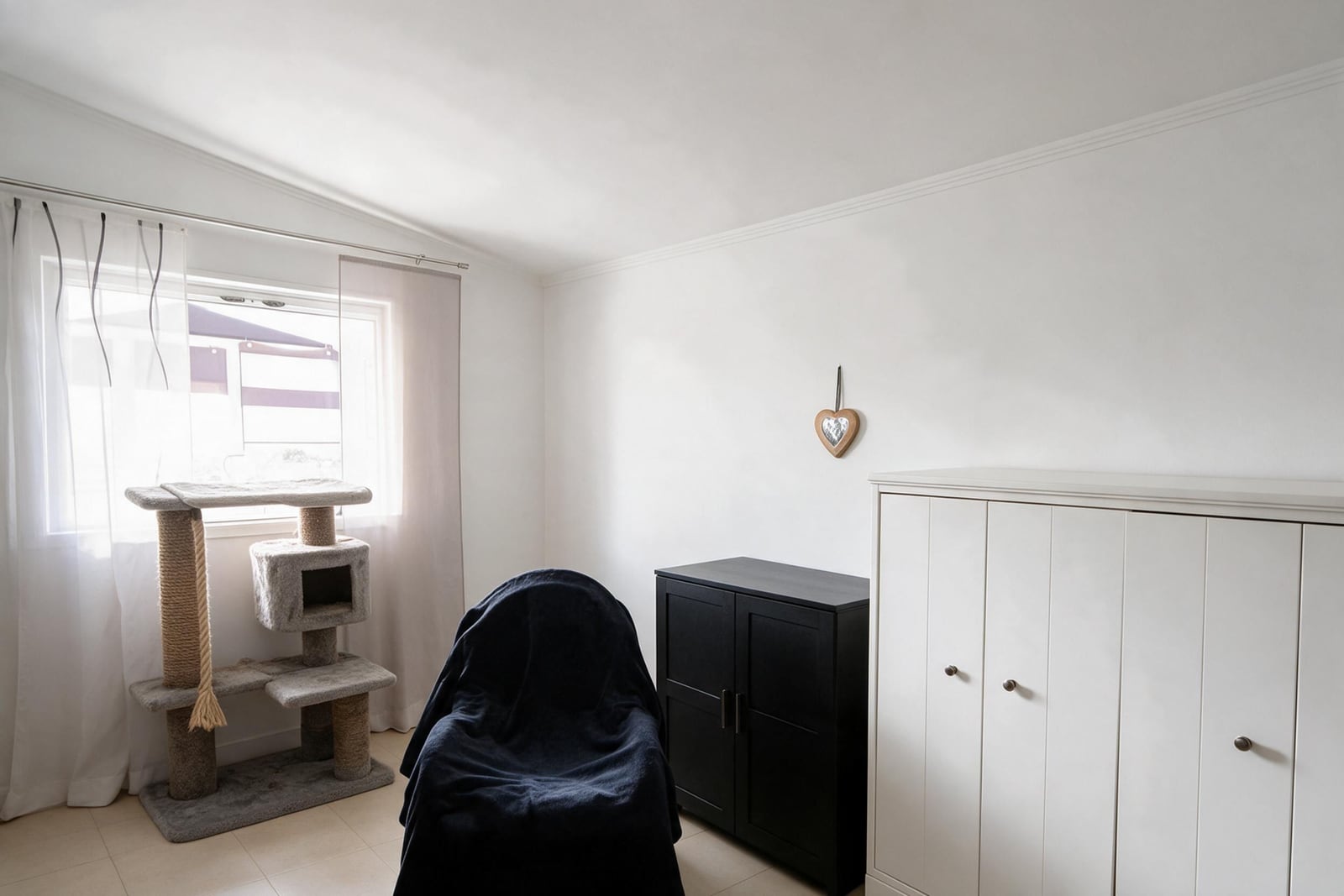 Room featuring a cat tree, white wardrobe, black cabinet, and a covered object near the window.