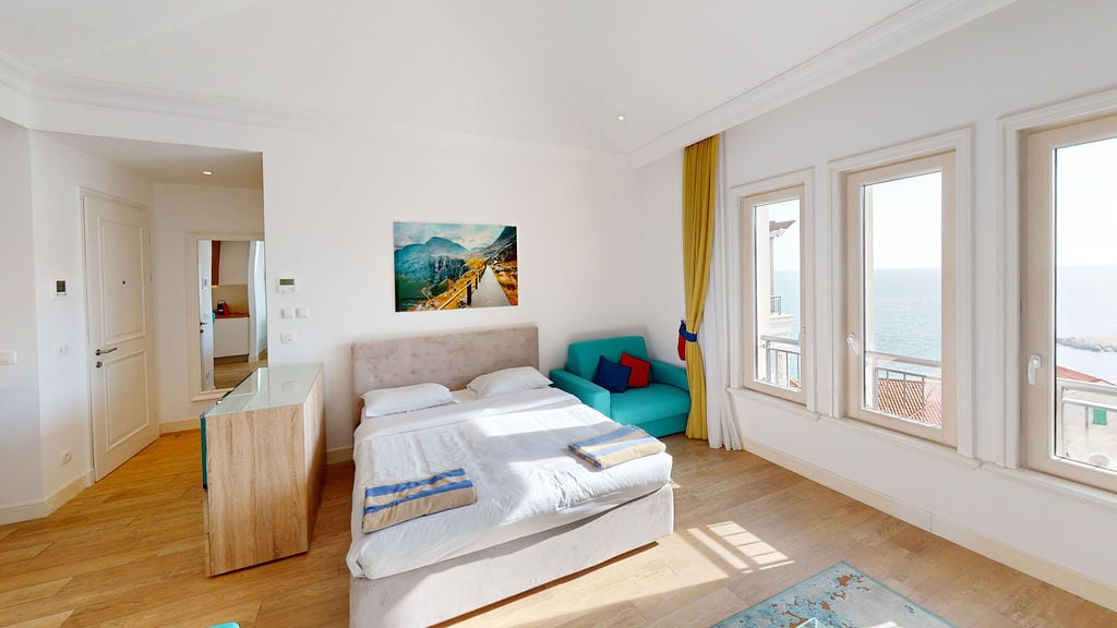 Bright bedroom in an apartment in Luštica, Montenegro: double bed, turquoise armchair, and panoramic sea view.