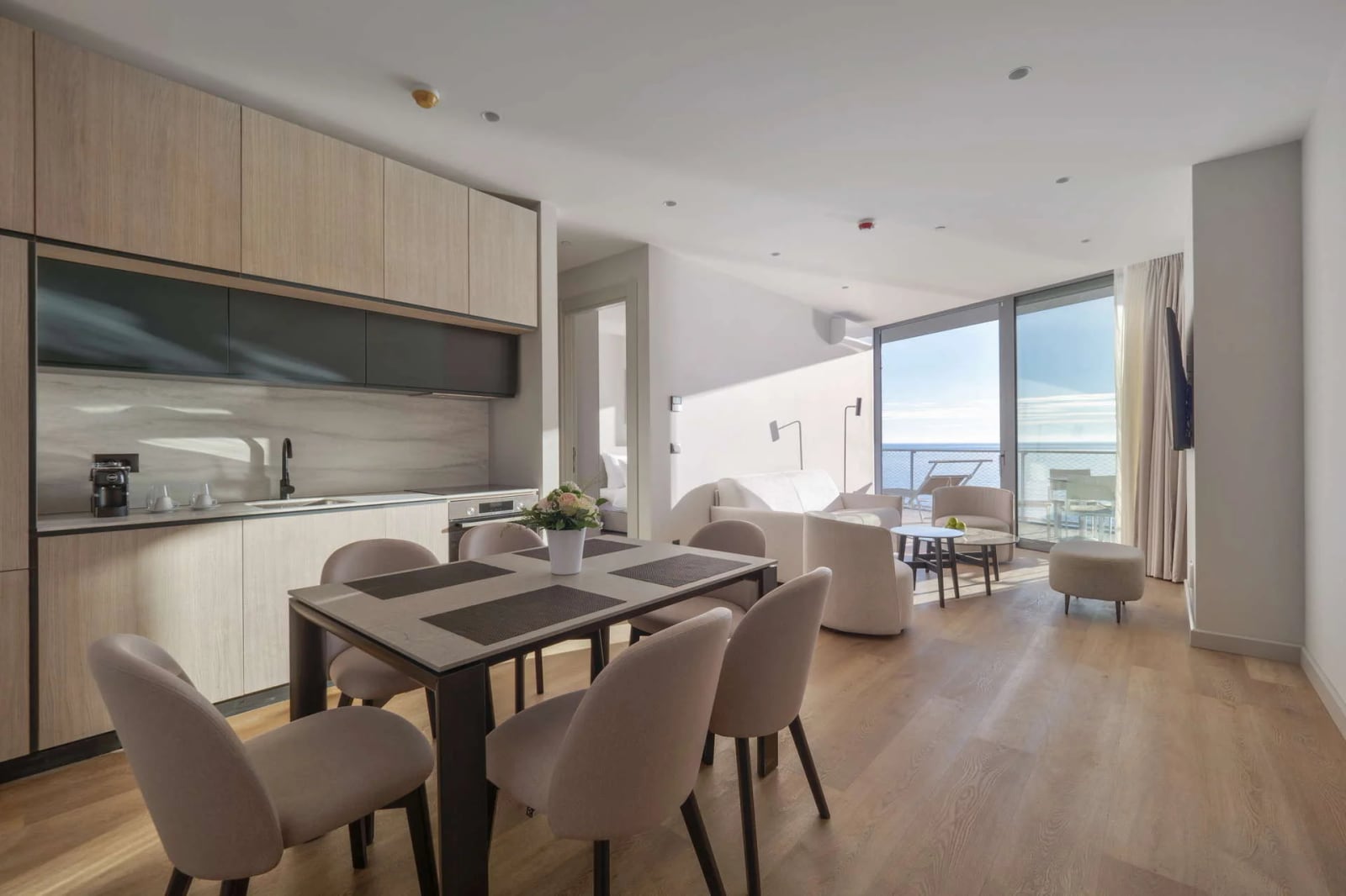 Living room with dining area and open kitchen, featuring ocean view through large glass windows.