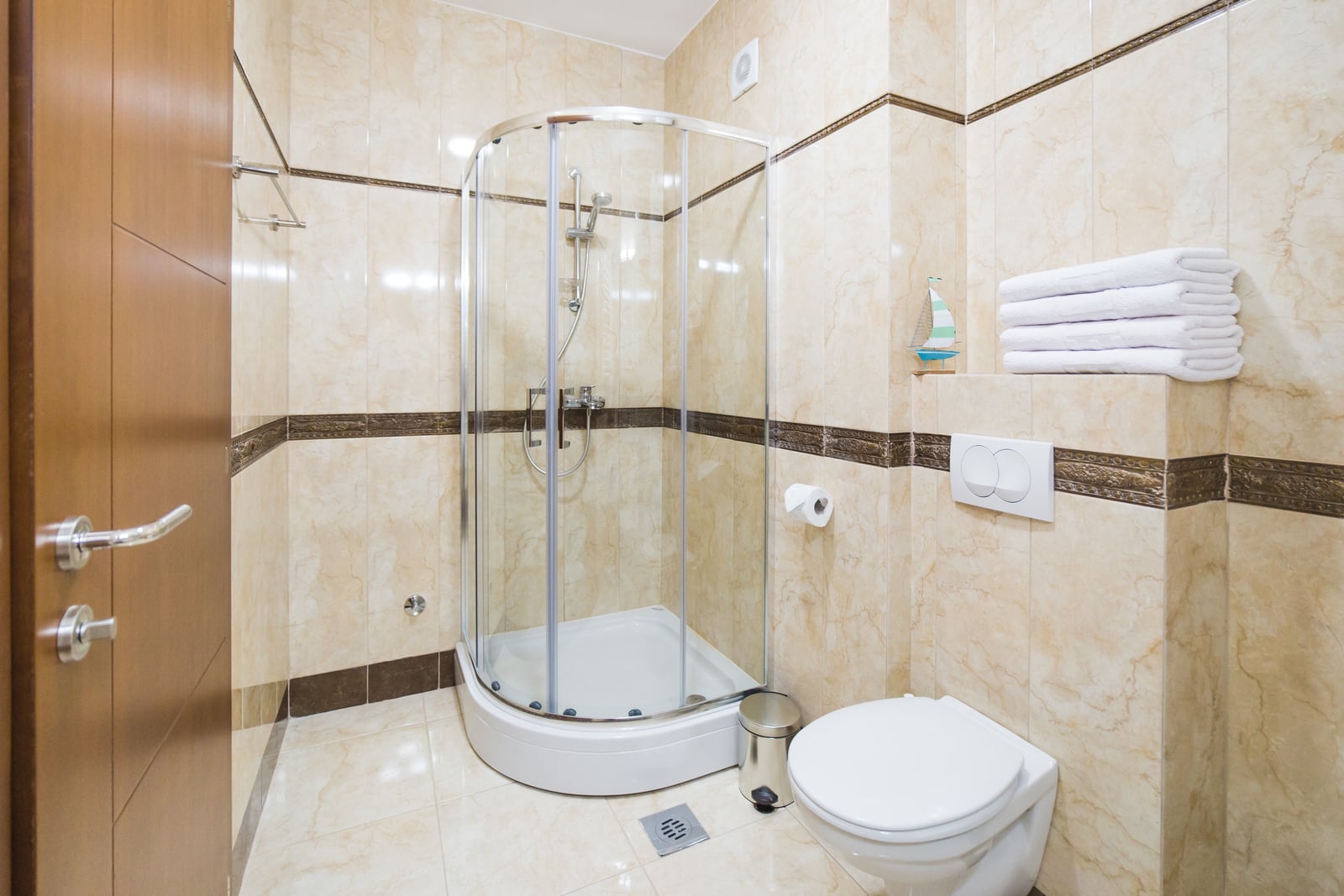 Bathroom in an apartment in Becici, Montenegro: shower cabin, wall-hung toilet, and beige tile interior.