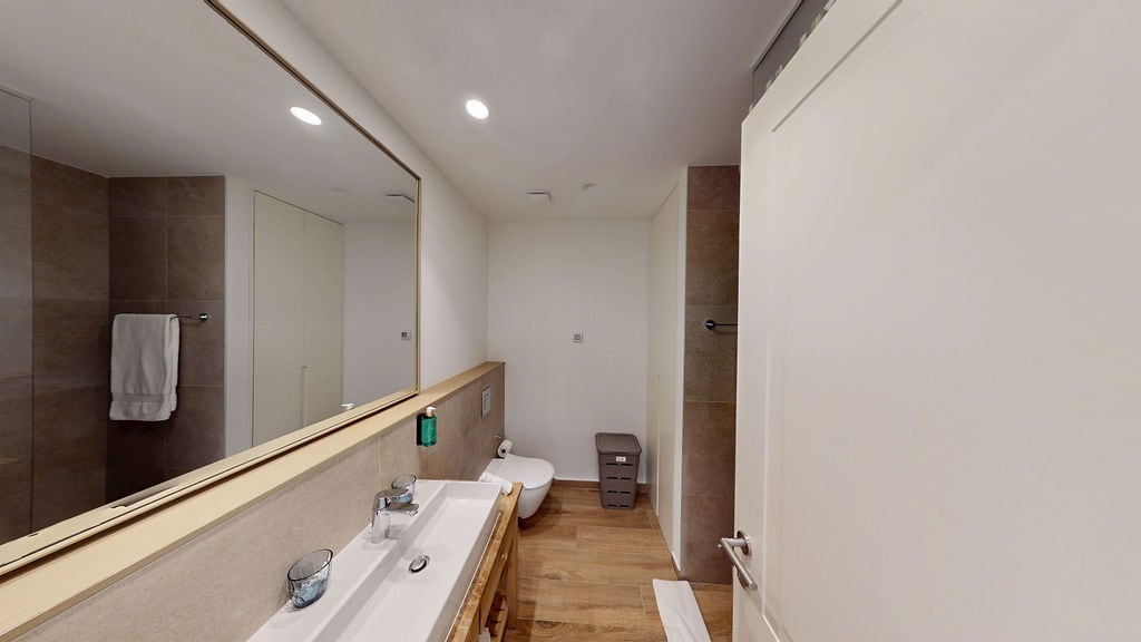 Modern bathroom in an apartment, Luštica, Montenegro: wood-effect tiles, large mirror, and plumbing fixtures.
