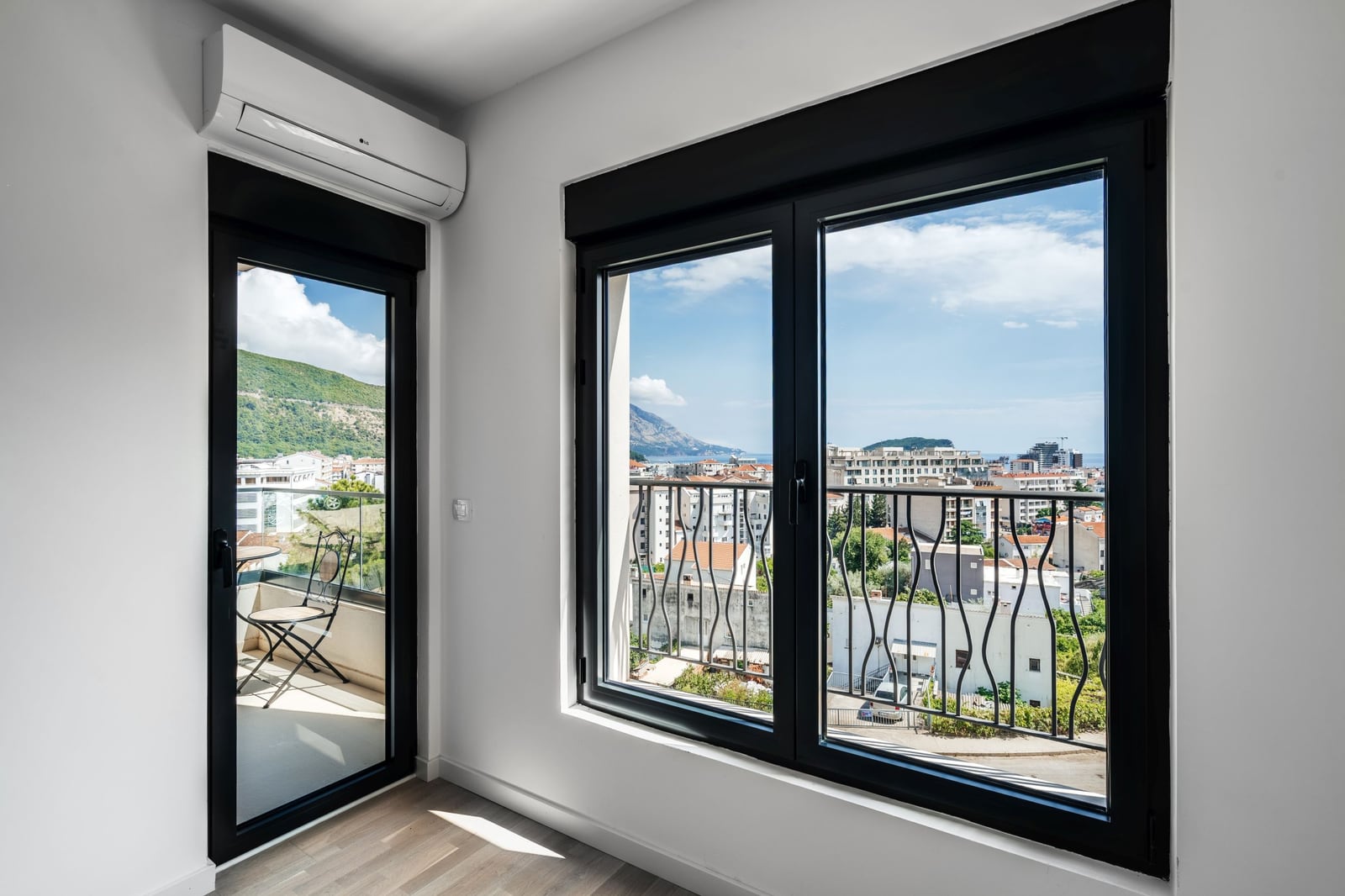 Living room with panoramic windows, access to the balcony, and a view of Budva, Montenegro. Modern interior.