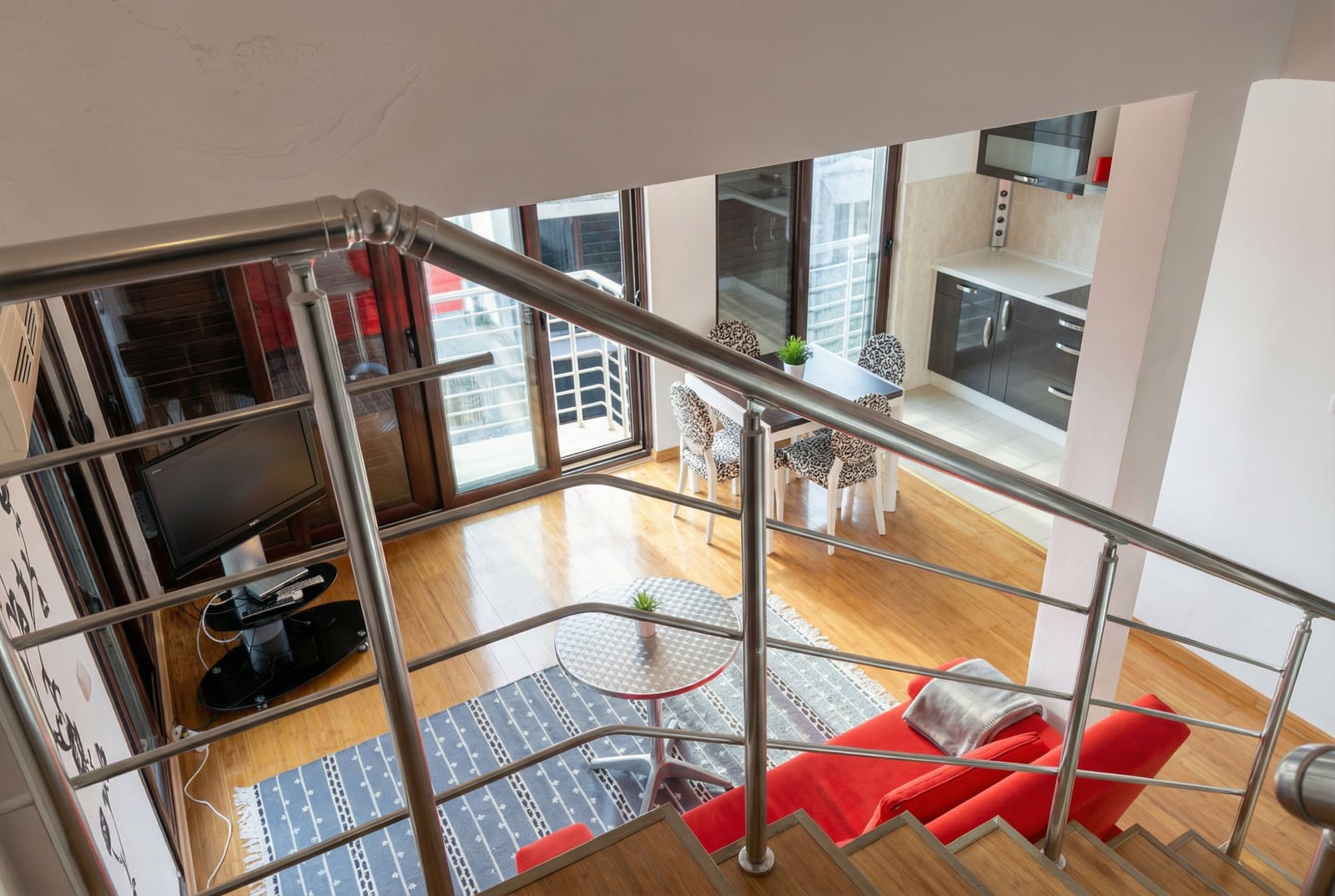 Interior of a duplex apartment in Bečići, Montenegro: view from the staircase of the living room with a red sofa and kitchen.