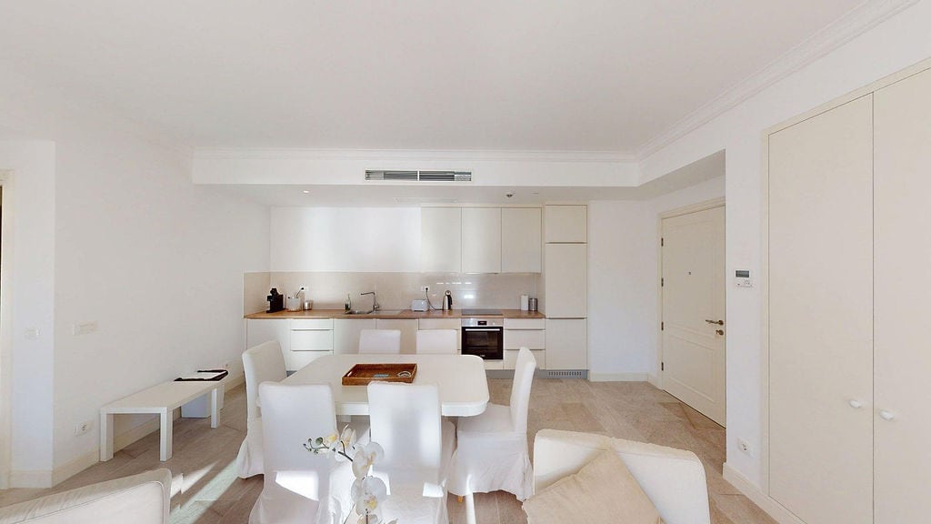 Modern light-toned kitchen-dining room in an apartment at Luštica residential complex, Montenegro: built-in appliances and dining area.