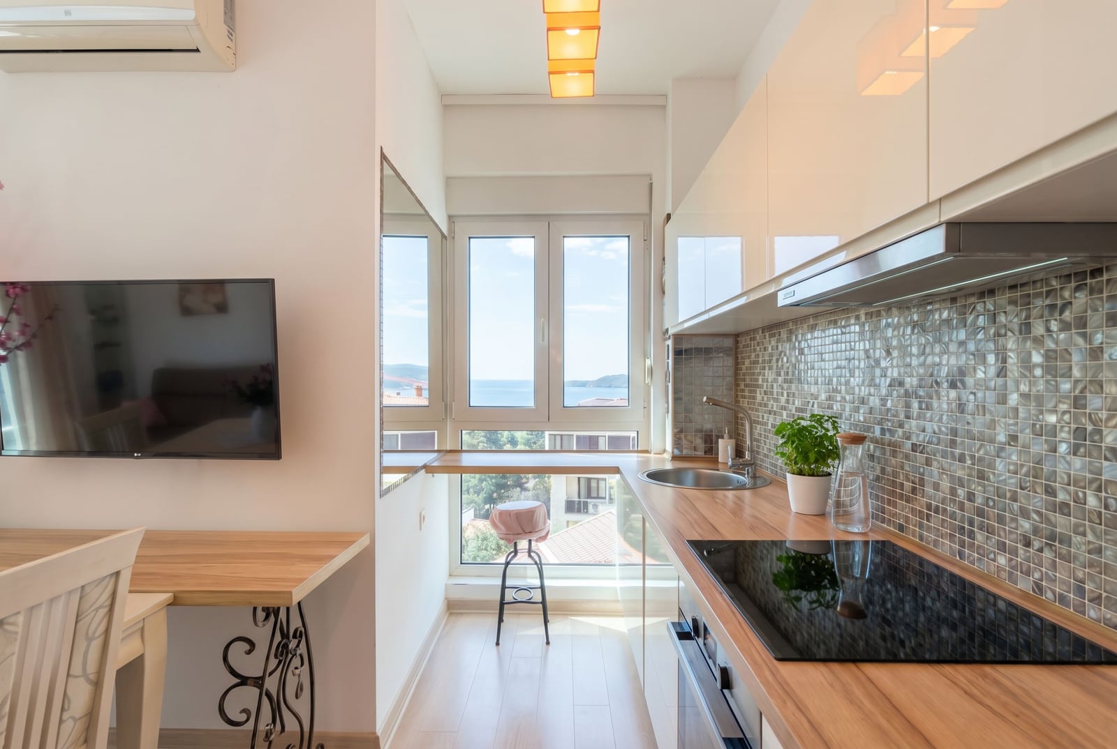 Modern kitchen in an apartment in Bečići, Montenegro: glossy fronts, sea view from the window, and a breakfast bar.