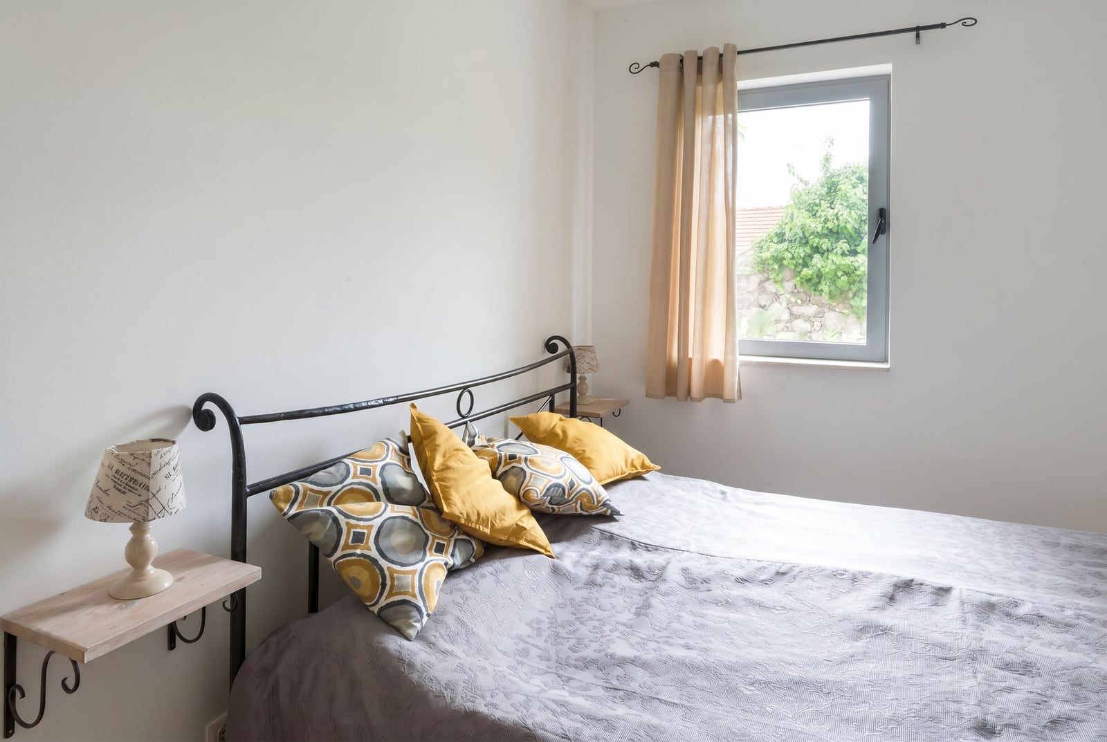 Bright bedroom with a wrought iron bed in an apartment in Risan, Montenegro: garden view, cozy interior, and bedside lamps.