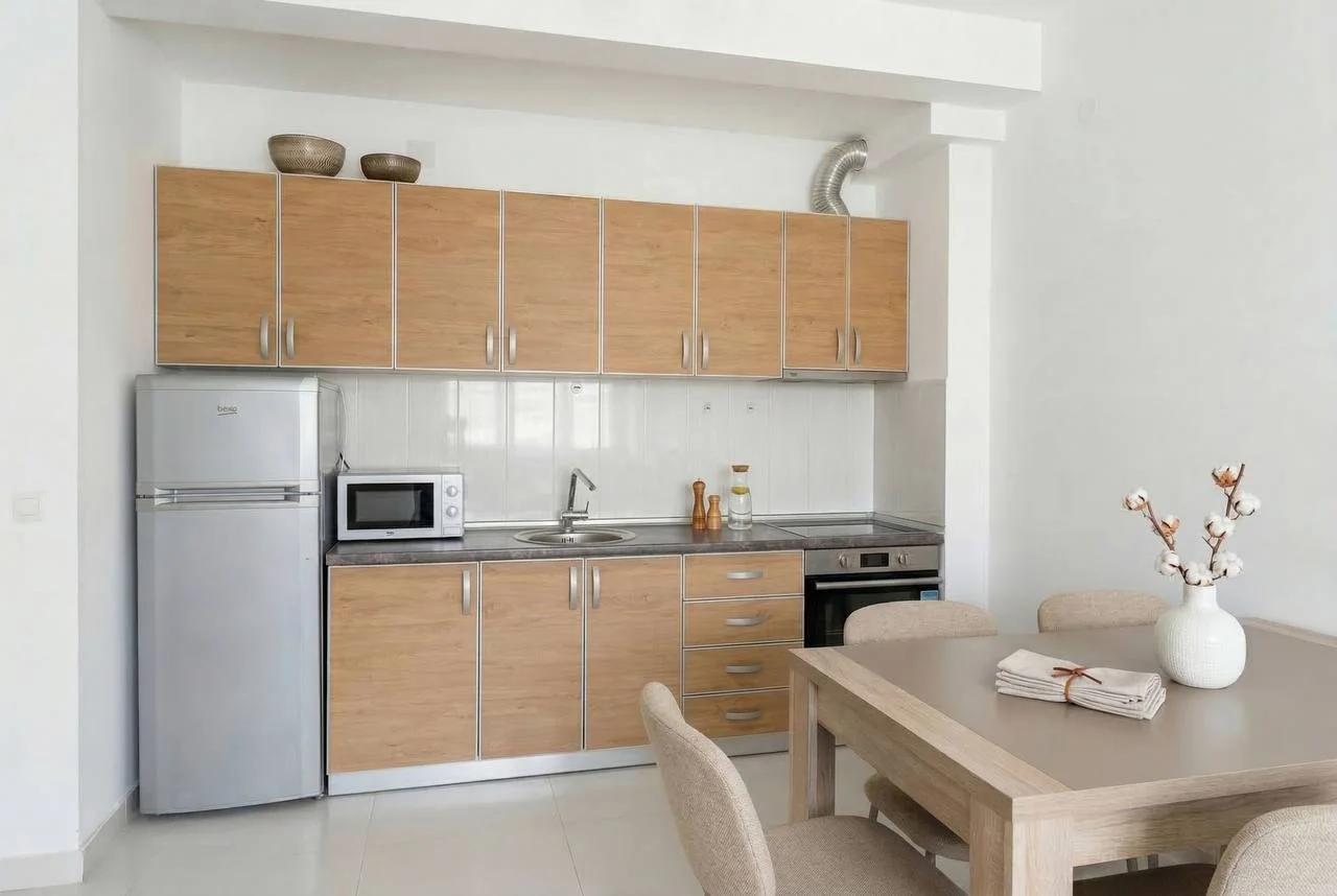 Modern kitchen with light wood cabinets, fridge, microwave, sink, and a dining table with chairs.