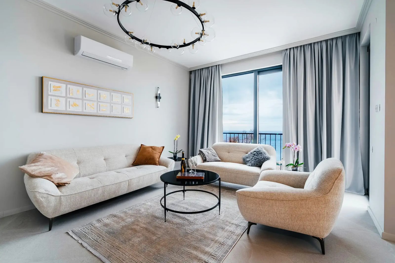 Bright living room with a sea view in a villa in Reževići, Montenegro: upholstered furniture, designer chandelier, and panoramic windows.