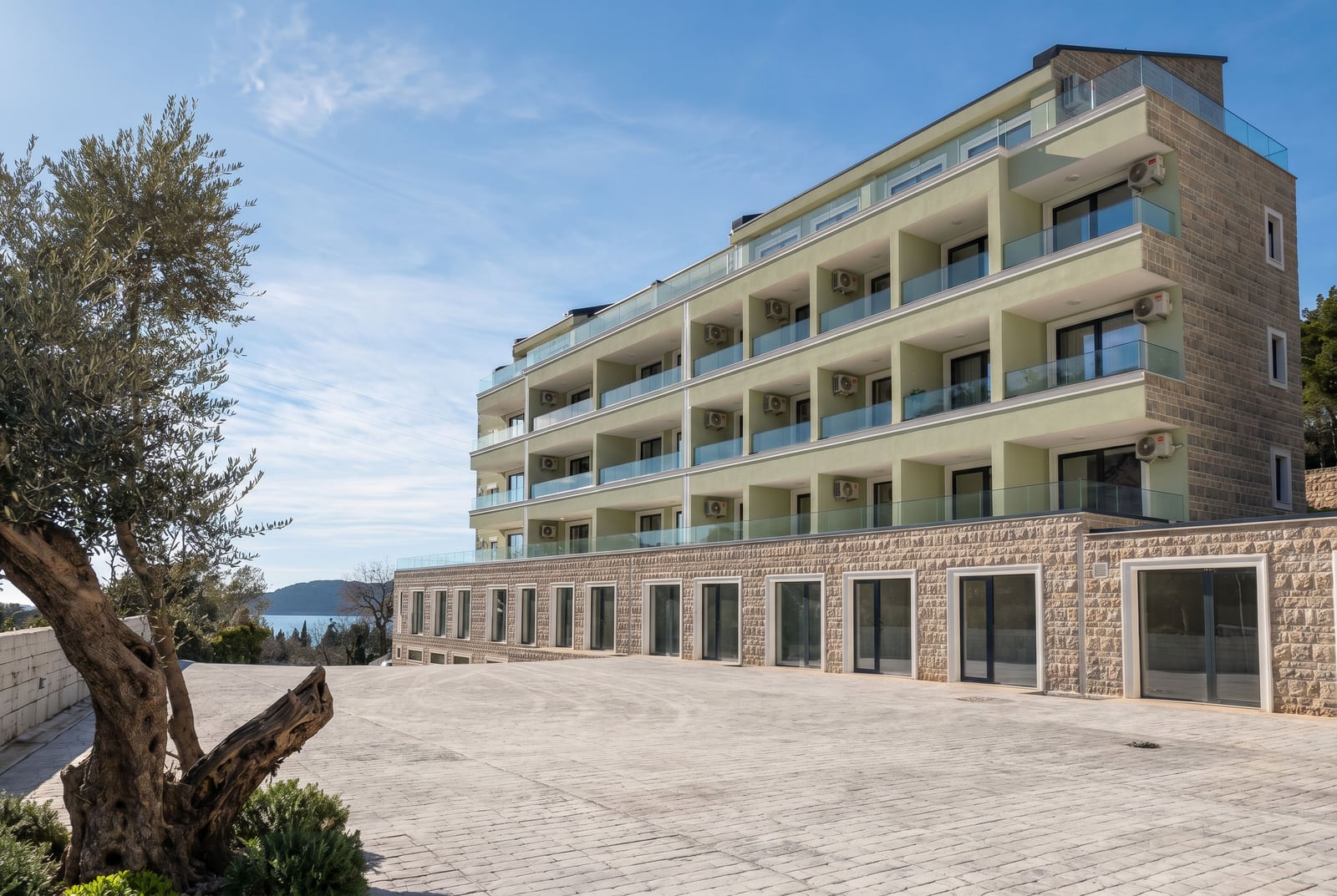 Modern residential complex with terraces in Pržno, Montenegro, view of the building with stone cladding and an olive tree.