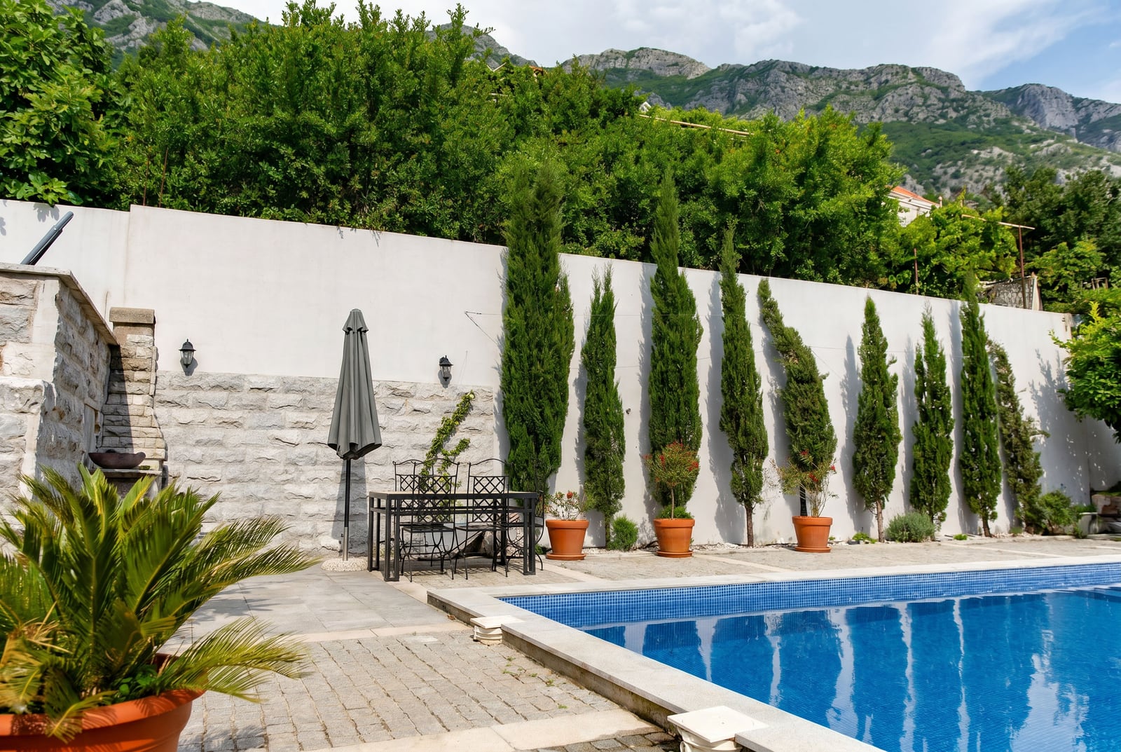 Outdoor pool with terrace, garden furniture, and cypress trees near a house in Risan, Montenegro.