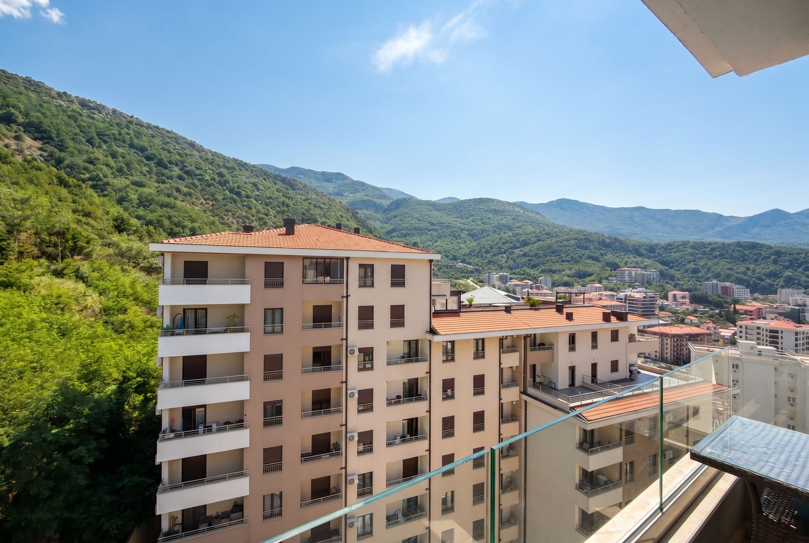 View from the apartment balcony in Bečići, Montenegro: a panorama of modern residential buildings and green mountains on a sunny day.
