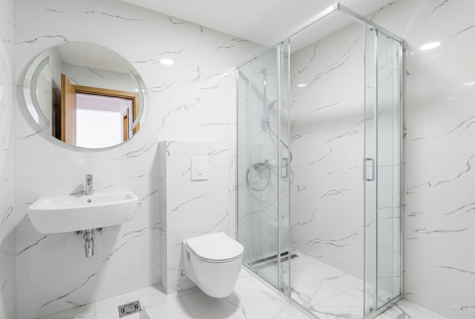 Modern bathroom in an apartment, Pržno, Montenegro: white marble-look tiles, shower cabin, and wall-hung toilet.