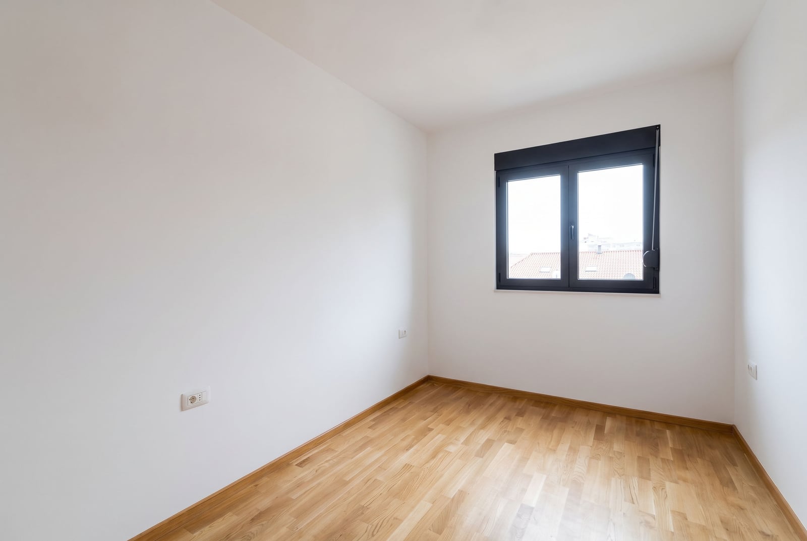 Bright empty bedroom with parquet flooring and a window in an apartment, Budva, Montenegro. Modern interior with white walls.