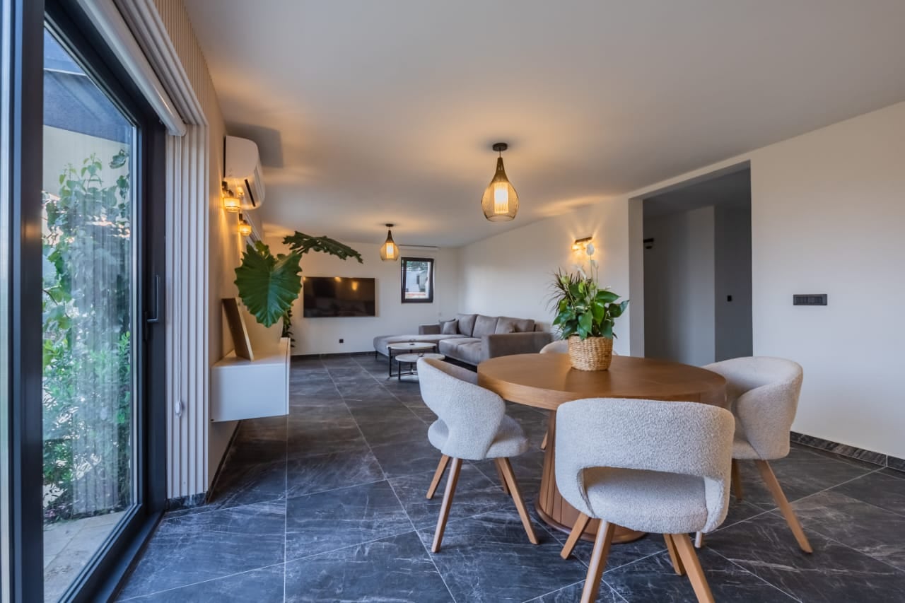 Modern living room with a dining area in a villa in Budva, Montenegro: panoramic windows, stylish furniture, and tile flooring.