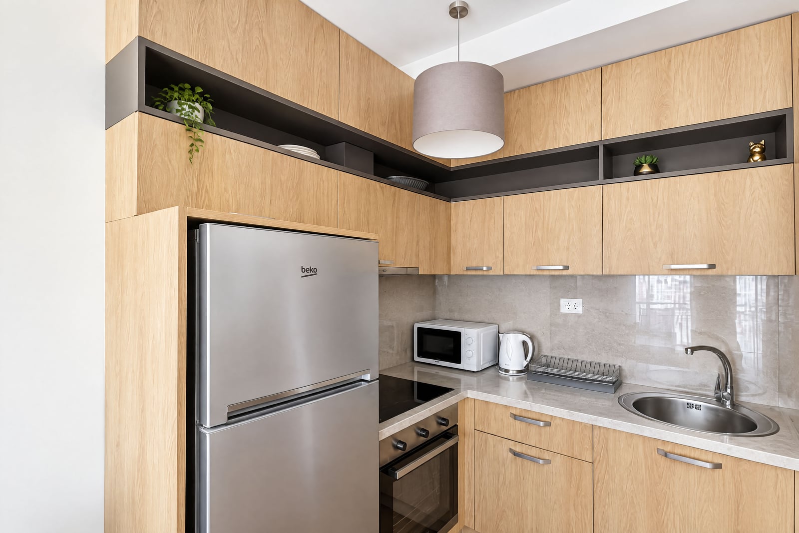 Modern kitchen with light wood cabinets, a Beko fridge, microwave, stove, sink, and pendant light.