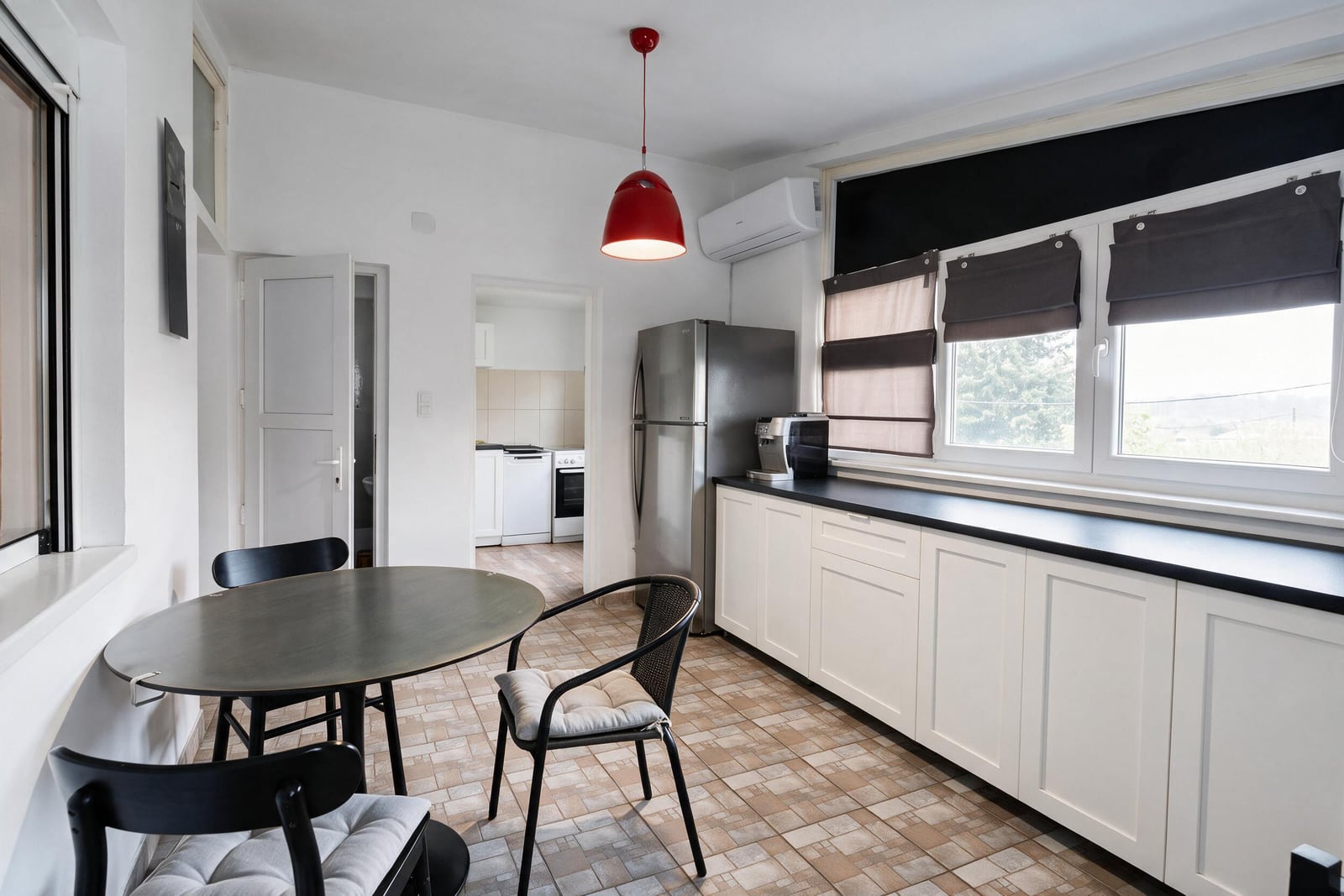 Kitchen with white cabinets, black countertop, stainless fridge, dining table, and red pendant light over tiled floor.