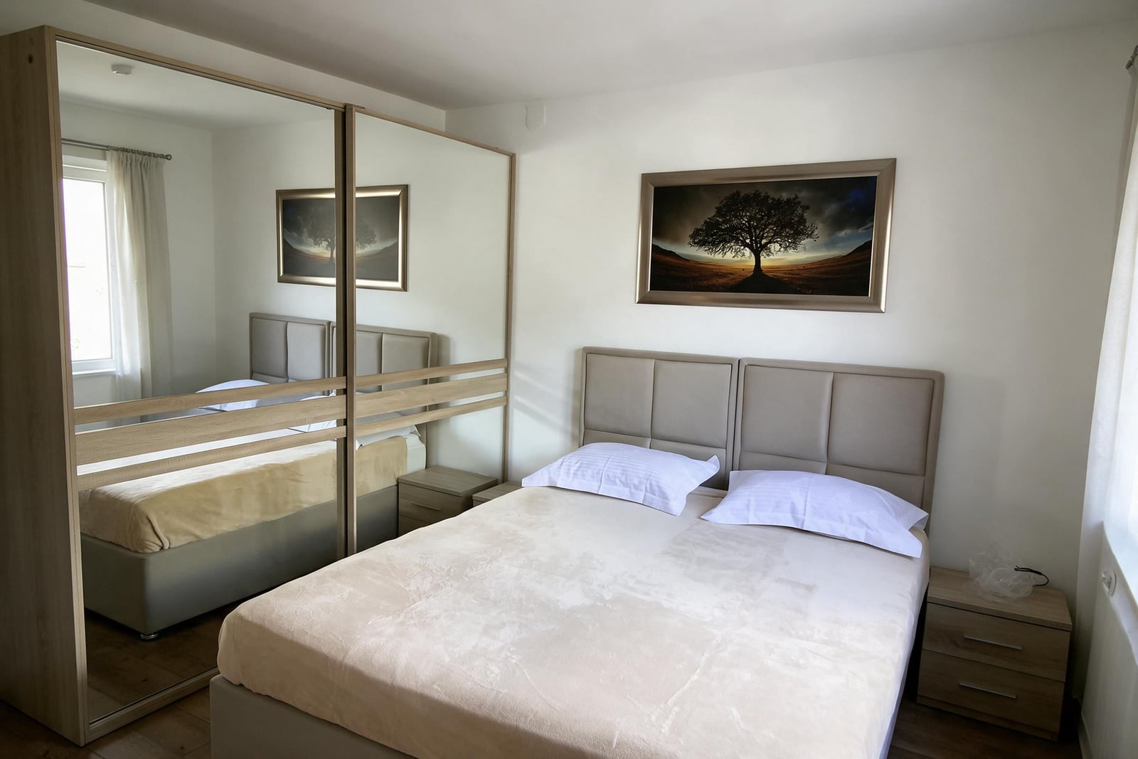 Bedroom featuring a double bed with beige bedding, mirrored wardrobe, and tree artwork on the wall.