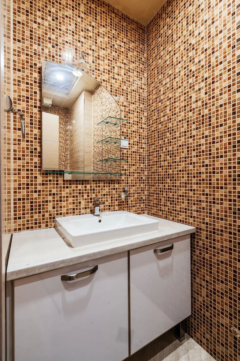 Bathroom in an apartment in Budva, Montenegro: a white vanity with sink and walls finished with brown mosaic.