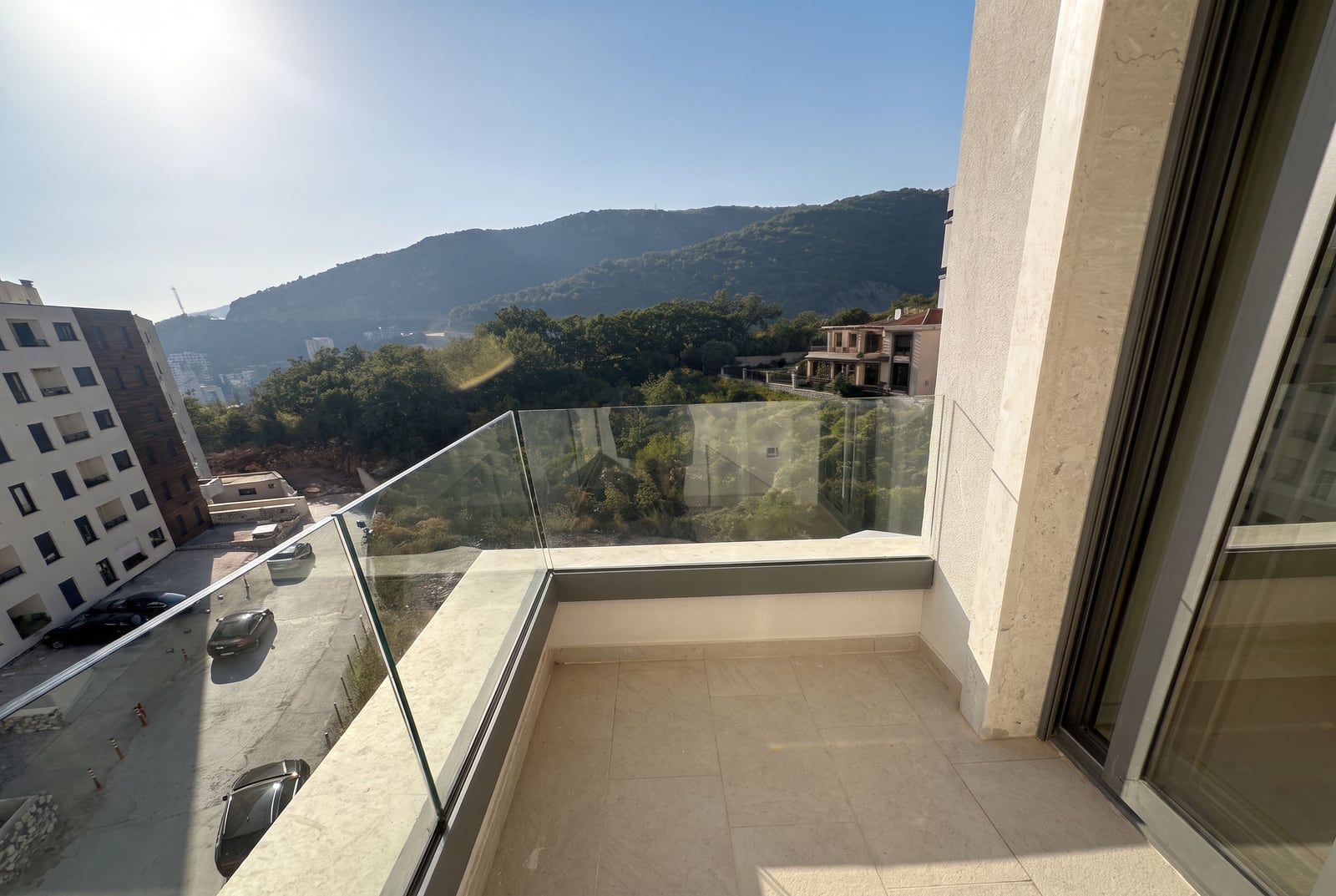 Empty balcony with glass railing overlooking mountains and city street.