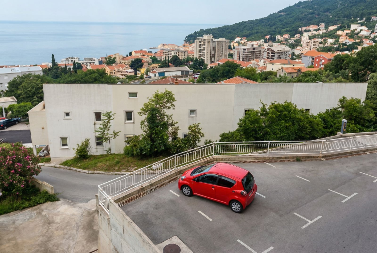 Parking at a residential complex in Petrovac, Montenegro, with panoramic views of the sea and city buildings.