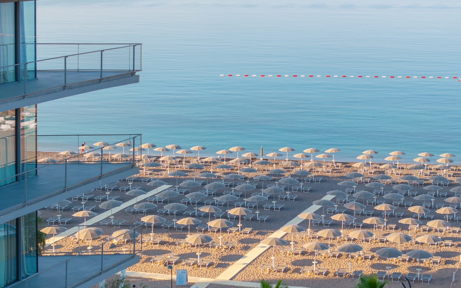 View from balconies overlooking a sandy beach with umbrellas and lounge chairs by the sea.