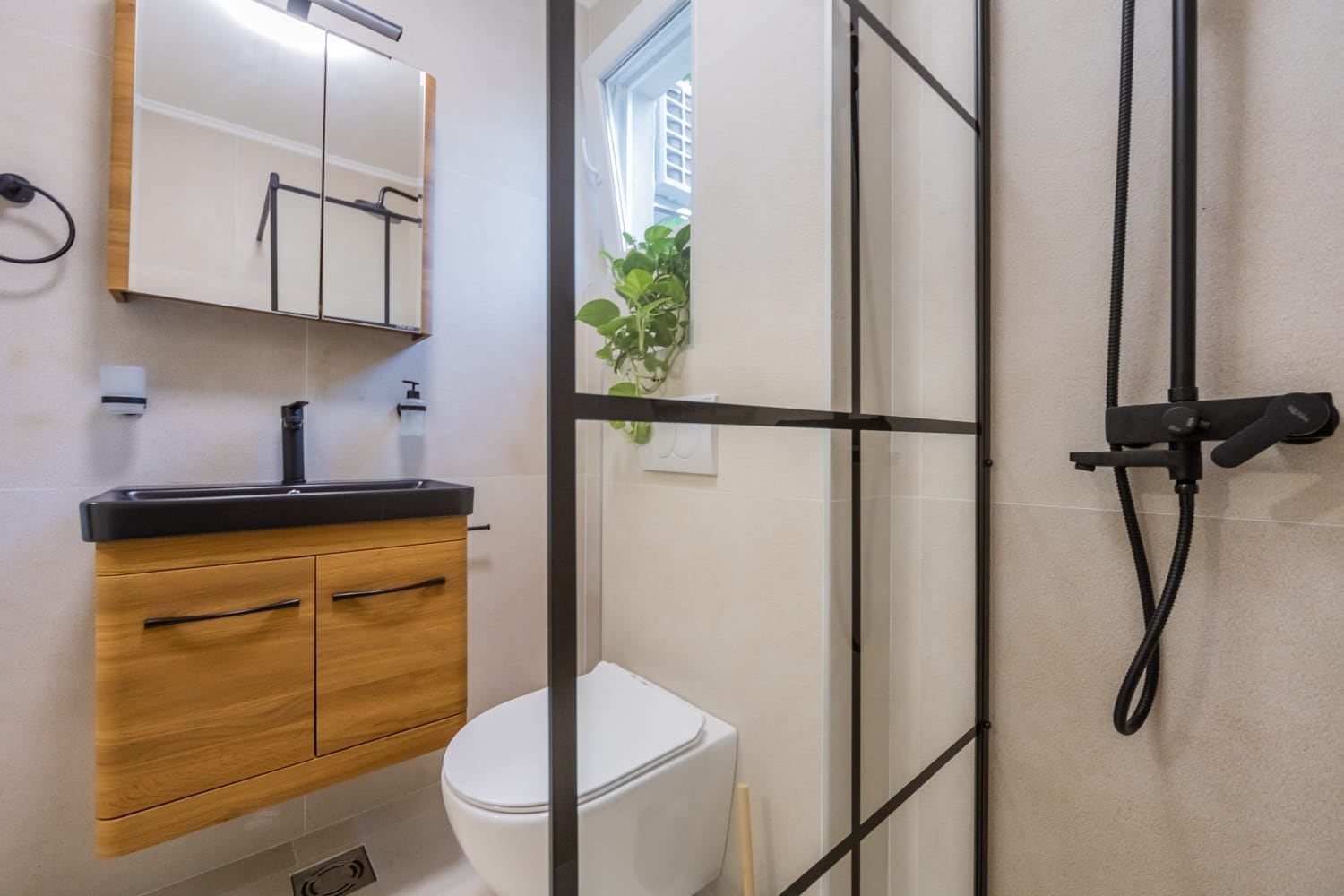 Modern bathroom in a villa in Budva, Montenegro: shower with black profile, wooden vanity unit, and light-colored tiles.