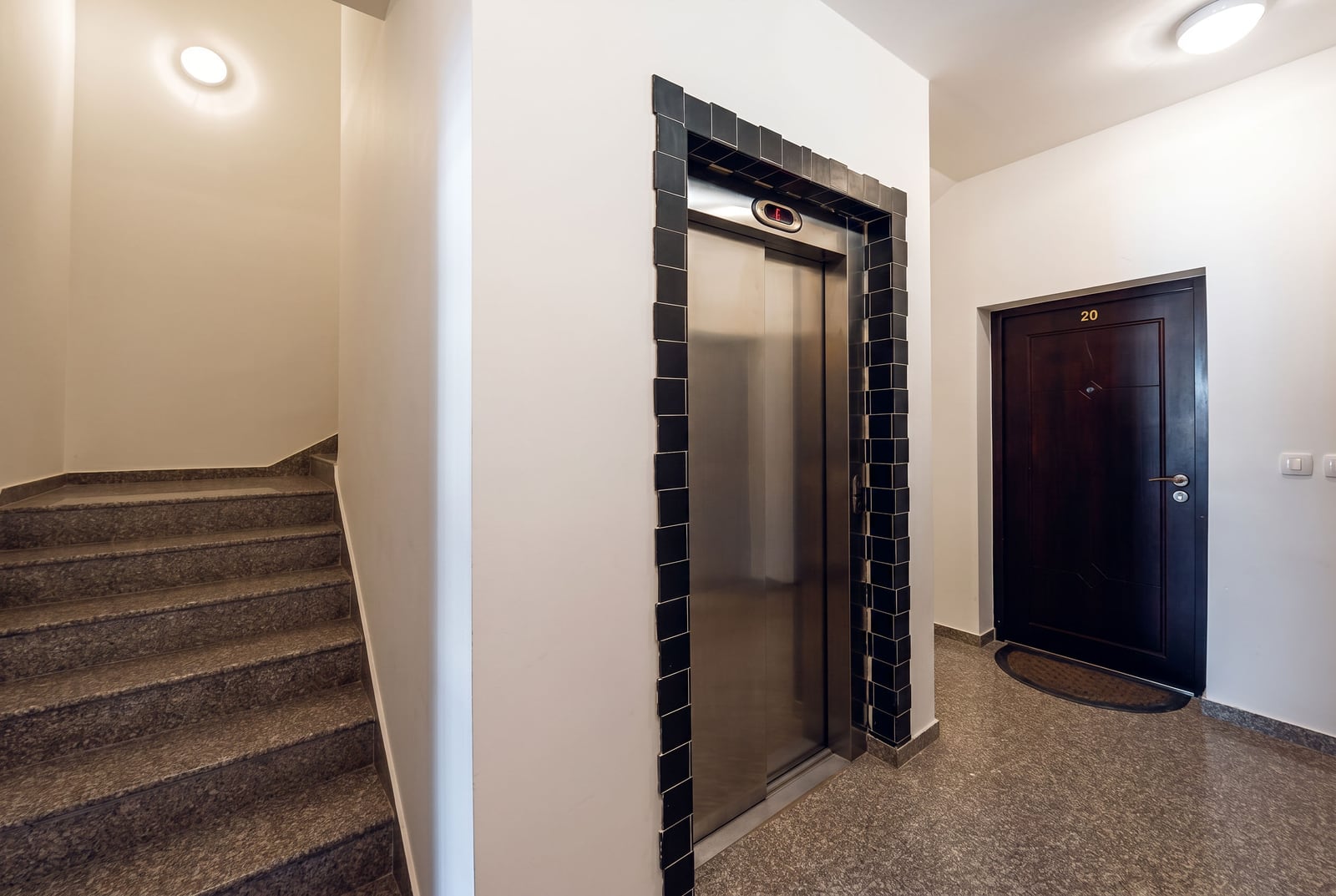 Modern entrance with an elevator and staircase in a residential building in Budva, Montenegro: tiled finish and apartment entrance door.