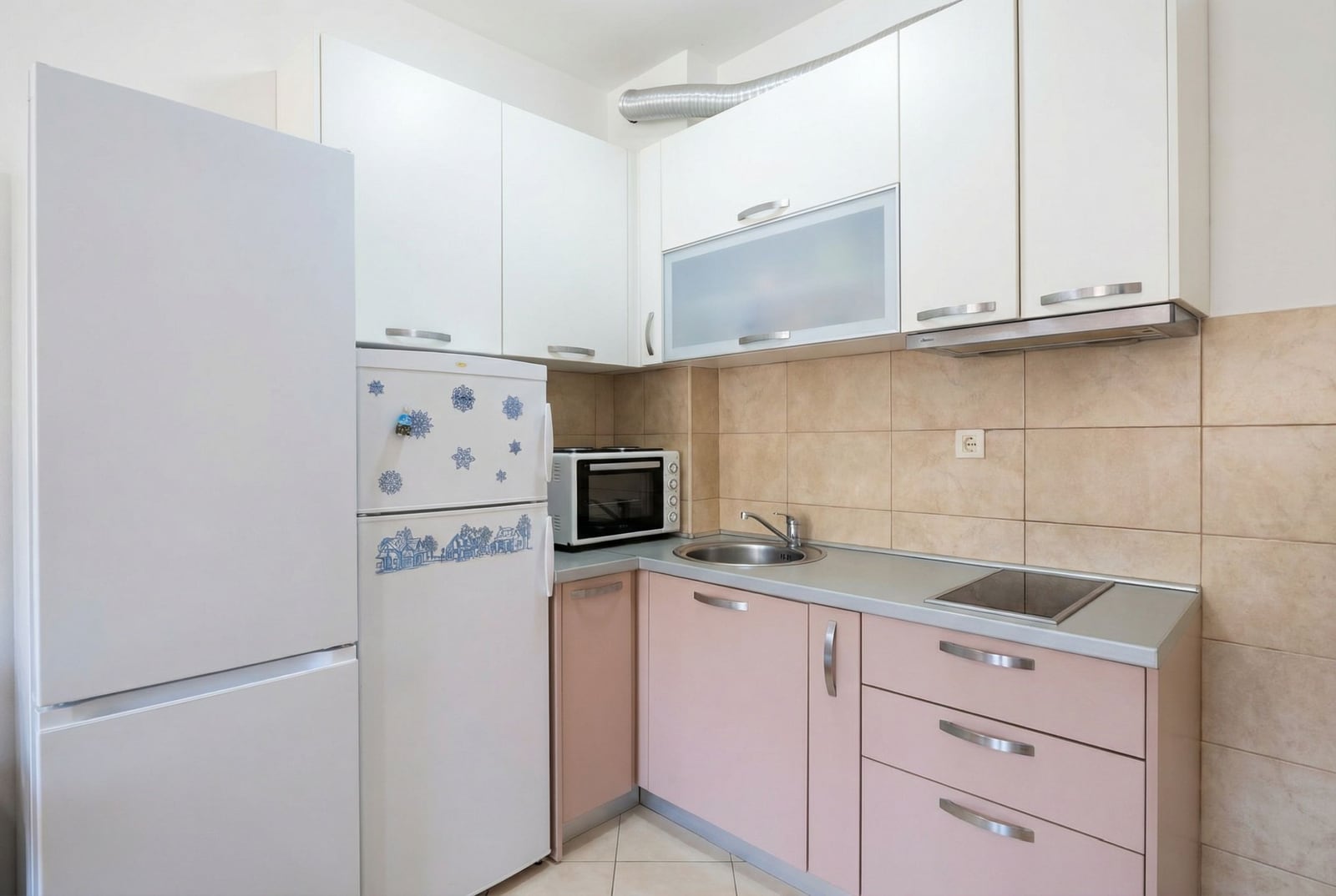 Compact kitchen in an apartment in Budva, Montenegro: white and pink cabinet fronts, built-in appliances, tiled backsplash.