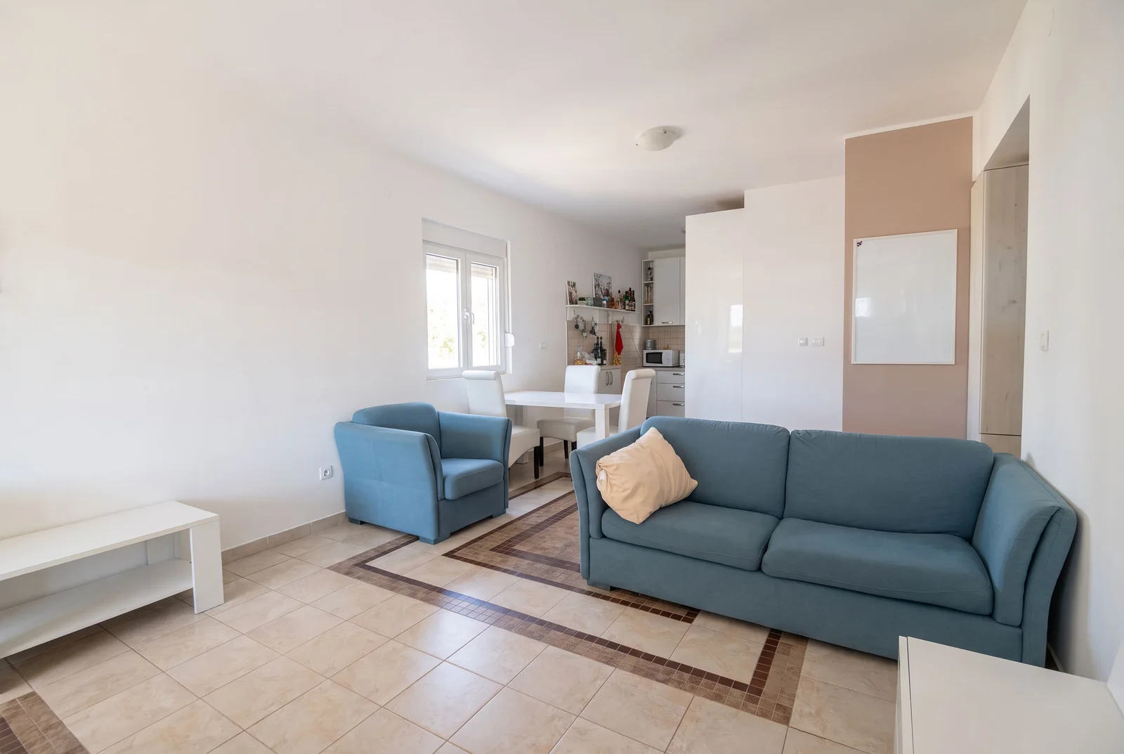 Living room featuring a blue sofa, armchair, white TV stand, and tiled flooring.