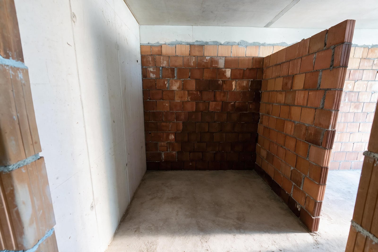 Unfinished room with red brick walls and concrete floor during the construction phase.