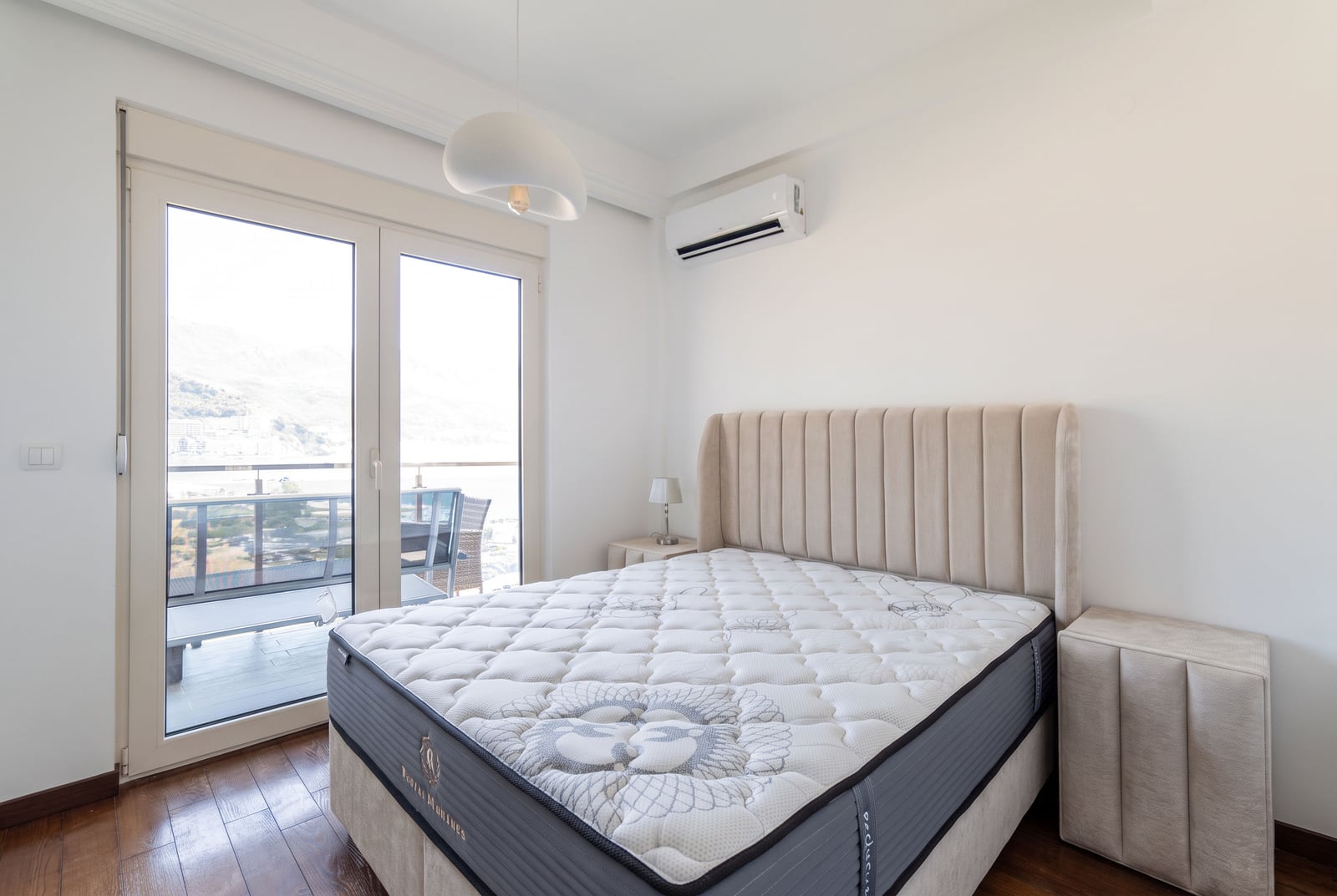 Bright bedroom featuring a large bed with an upholstered headboard and glass doors leading to a balcony.