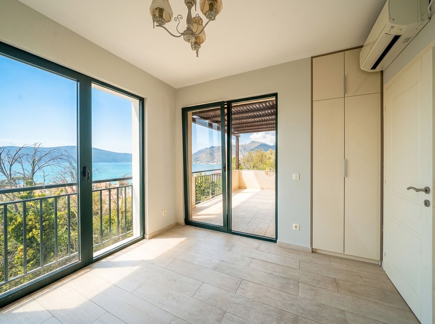 Empty room with tiled floor, built-in wardrobe, and large windows offering a sea view and access to a balcony.