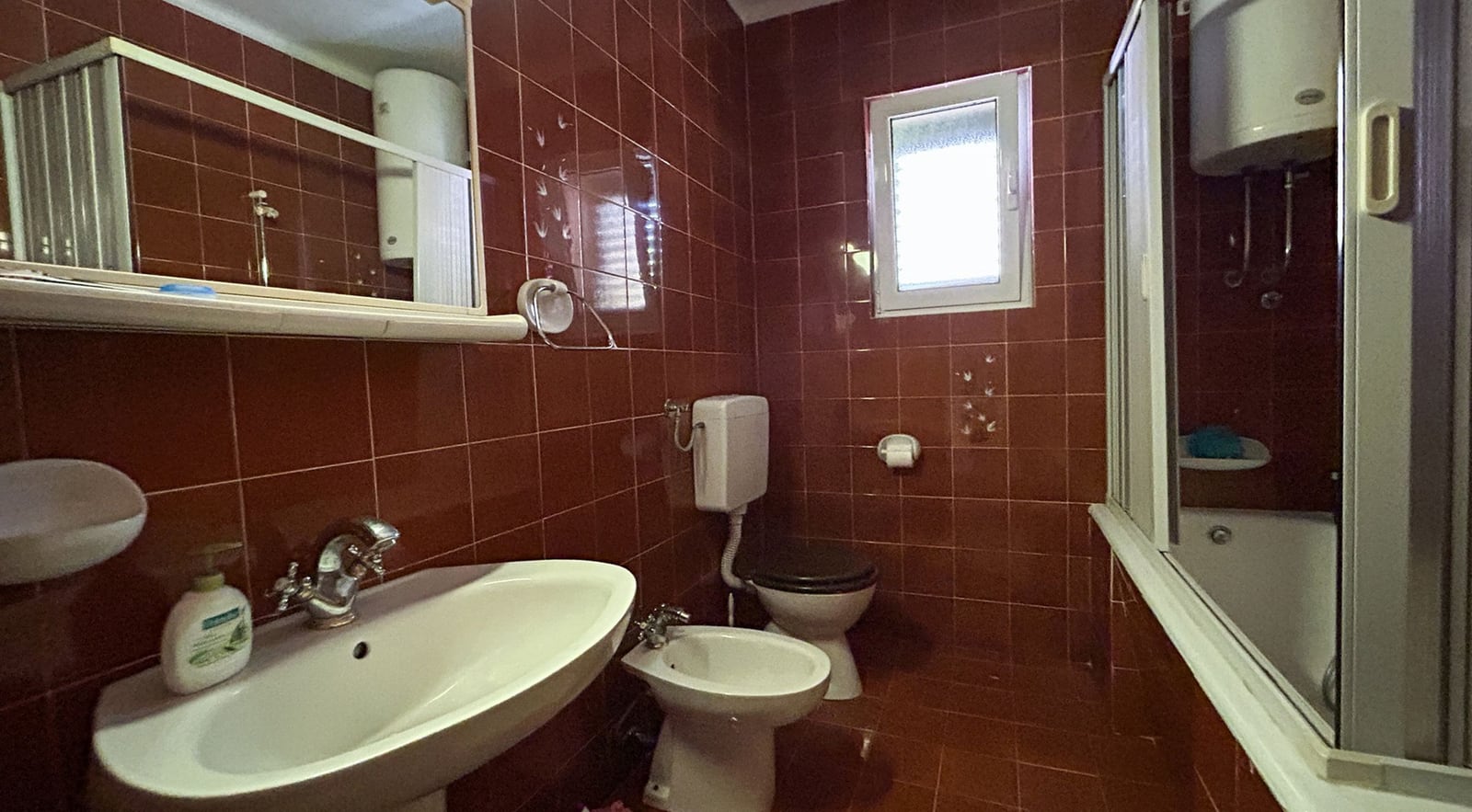Bathroom with brown tiles, a shower cabin, and a bidet in a villa in Dobrota, Montenegro.