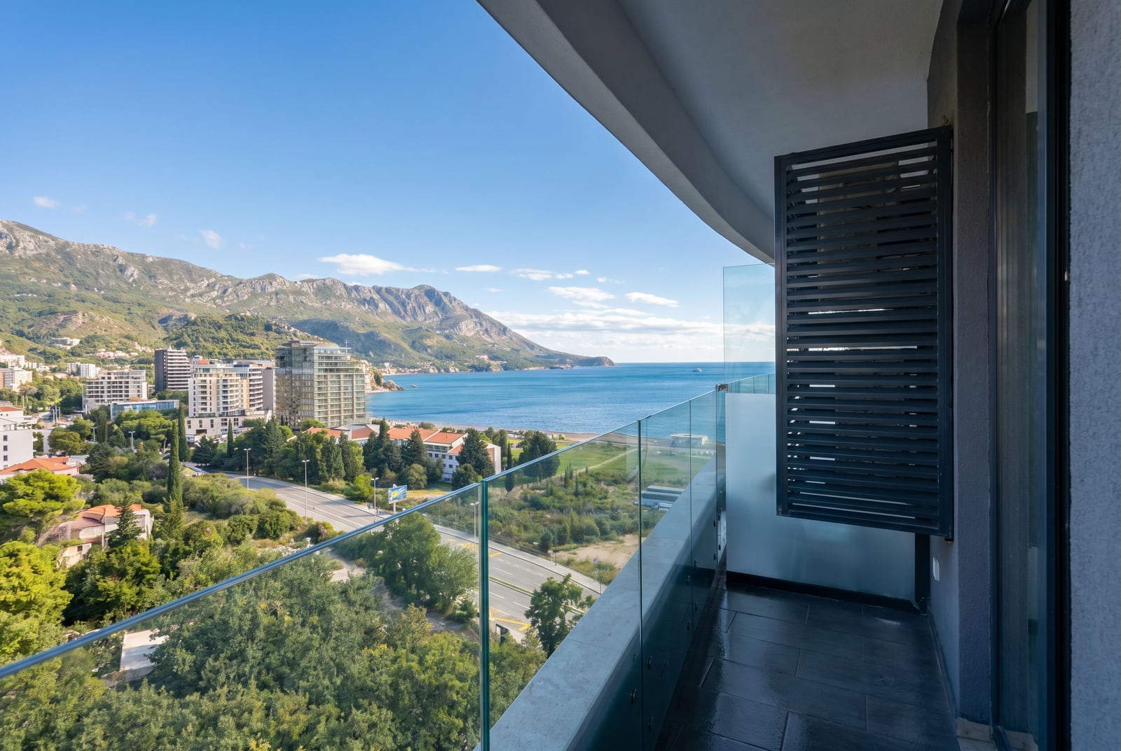 Balcony with a panoramic view of the sea and mountains in an apartment, Becici, Montenegro: glass railing, tiled floor, modern residential complex.