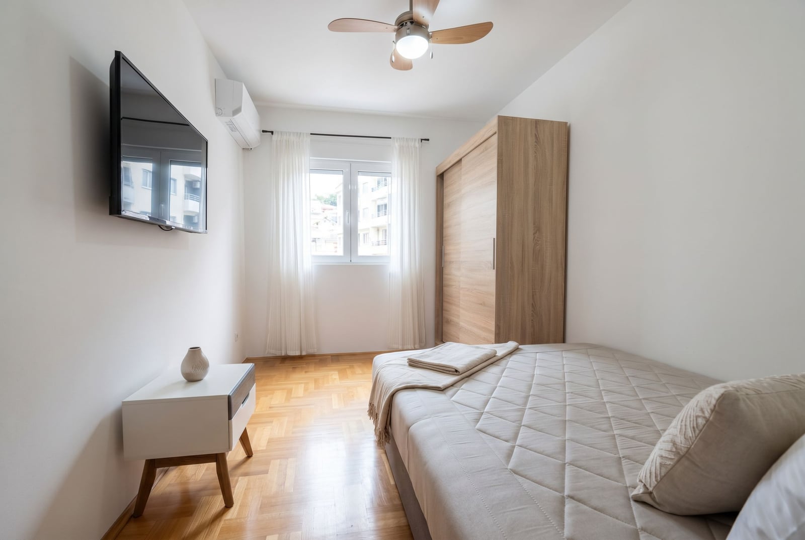 Cozy bedroom with a double bed and wardrobe in an apartment for sale in Budva, Montenegro. Parquet flooring, air conditioning, TV.